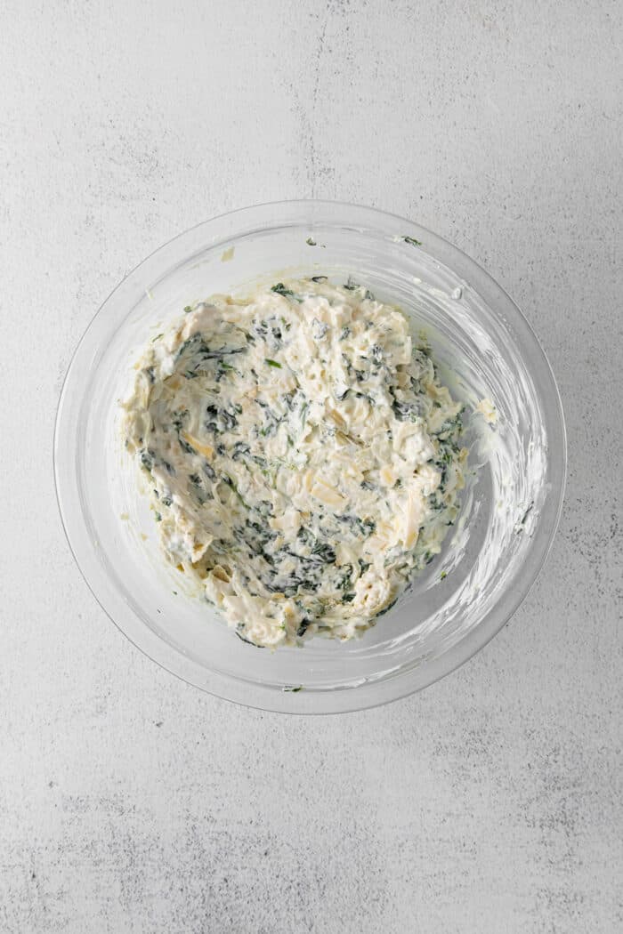 Creamy and cheesy, this baked Spinach Artichoke Dip recipe is a classic party dip. Serve hot with chips, pita, or veggies. Irresistible! Spinach and artichoke dip mixture in a bowl