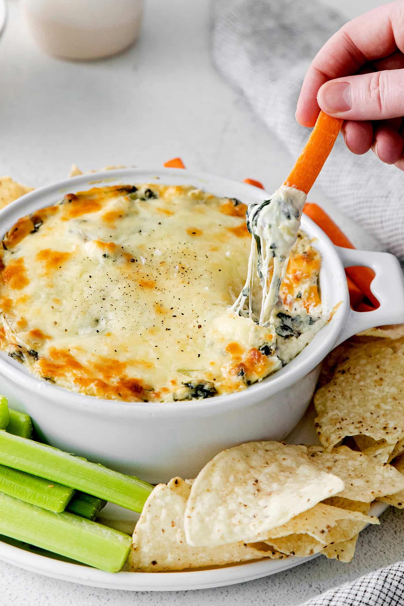 Creamy and cheesy, this baked Spinach Artichoke Dip recipe is a classic party dip. Serve hot with chips, pita, or veggies. Irresistible! Overhead view of a hand dipping a carrot into spinach artichoke dip