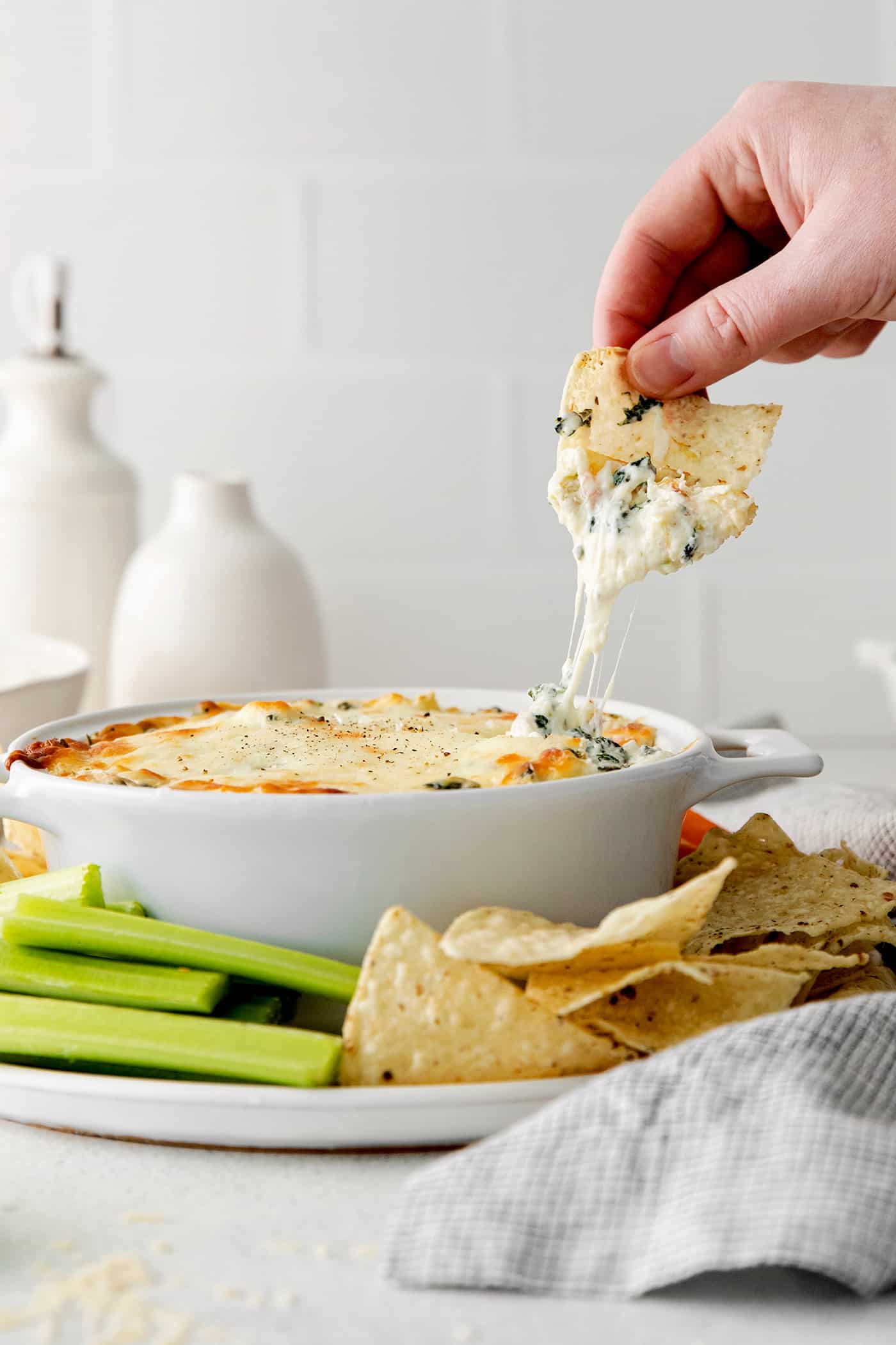 Creamy and cheesy, this baked Spinach Artichoke Dip recipe is a classic party dip. Serve hot with chips, pita, or veggies. Irresistible! A hand dipping a chip into spinach artichoke dip