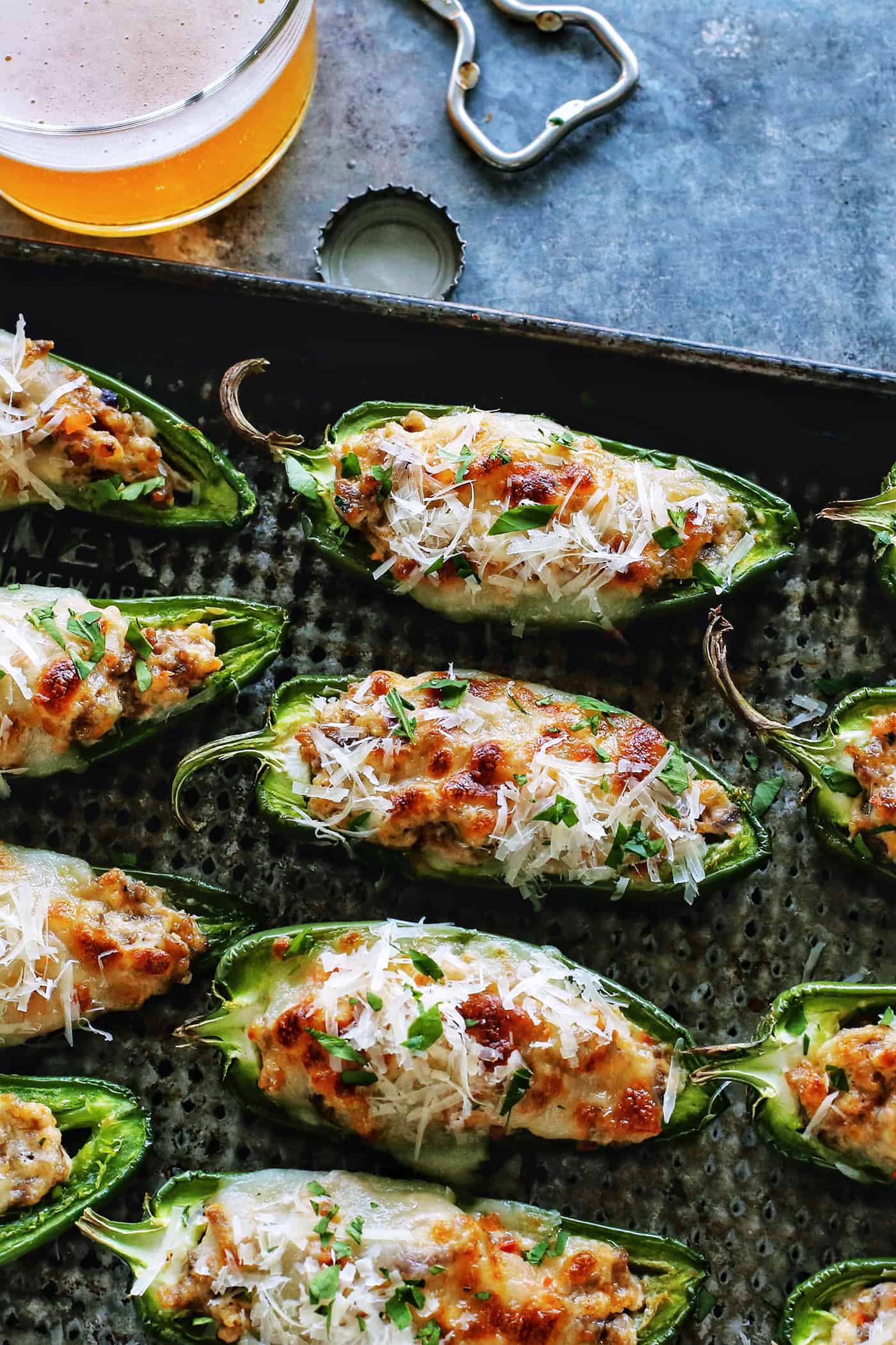 With Italian sausage, cream cheese, Parmesan, and mozzarella, these easy stuffed jalapeños are extra cheesy with the perfect amount of heat! baked stuffed jalapenos with sausage and cheese on a pan, plus a glass of beer