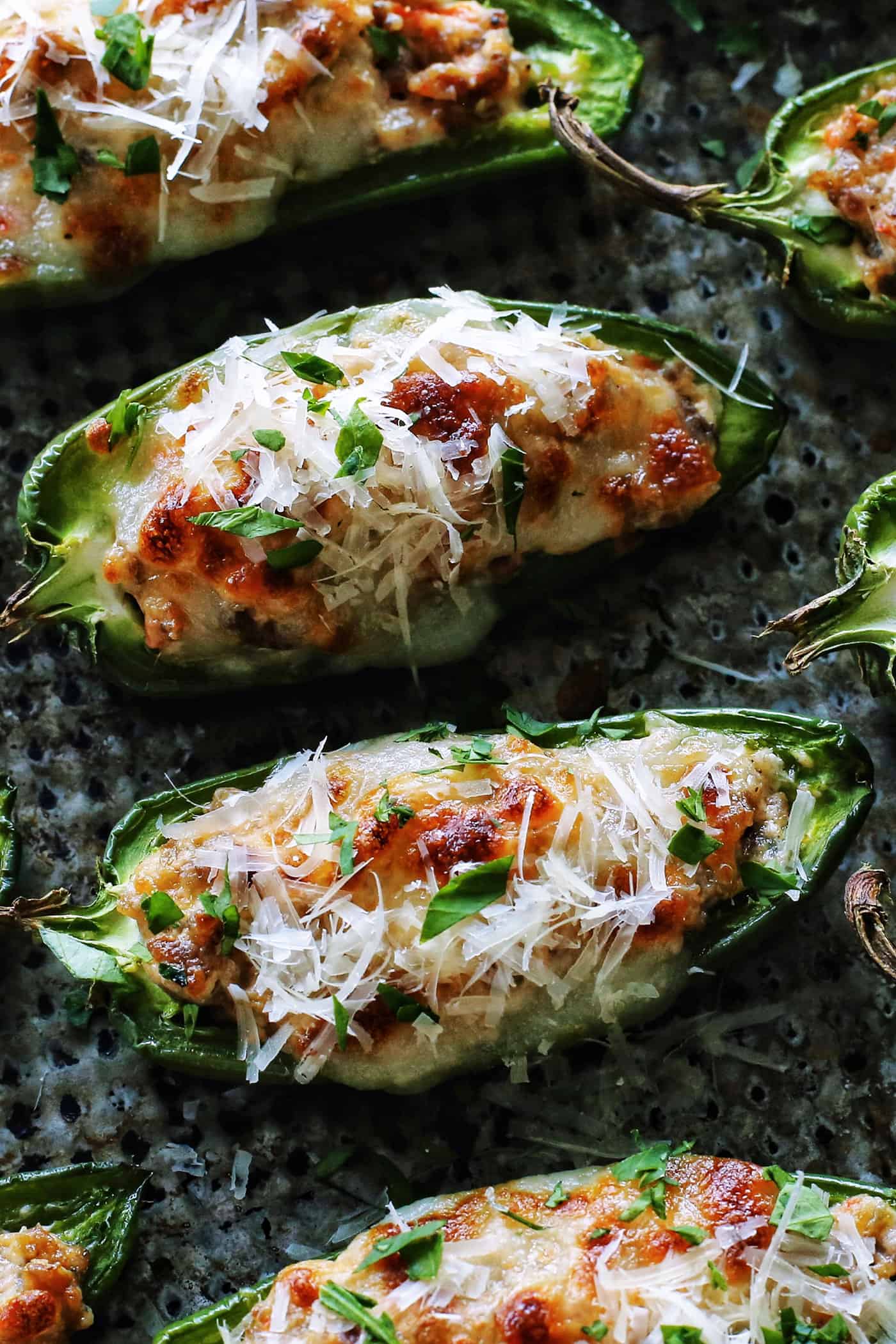 With Italian sausage, cream cheese, Parmesan, and mozzarella, these easy stuffed jalapeños are extra cheesy with the perfect amount of heat! close-up overhead photo of baked stuffed jalapeno peppers