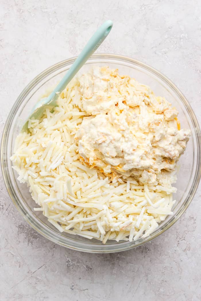 This cheesy hashbrown casserole recipe is an easy side dish that’s ready in under an hour. You'll love the crispy cornflake topping! Hashbrowns and sauce ingredients in glass bowl with spoon
