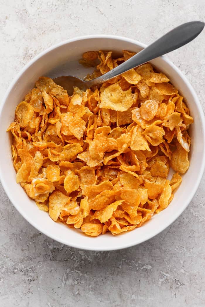 This cheesy hashbrown casserole recipe is an easy side dish that’s ready in under an hour. You'll love the crispy cornflake topping! Cornflake mixture in bowl with spoon