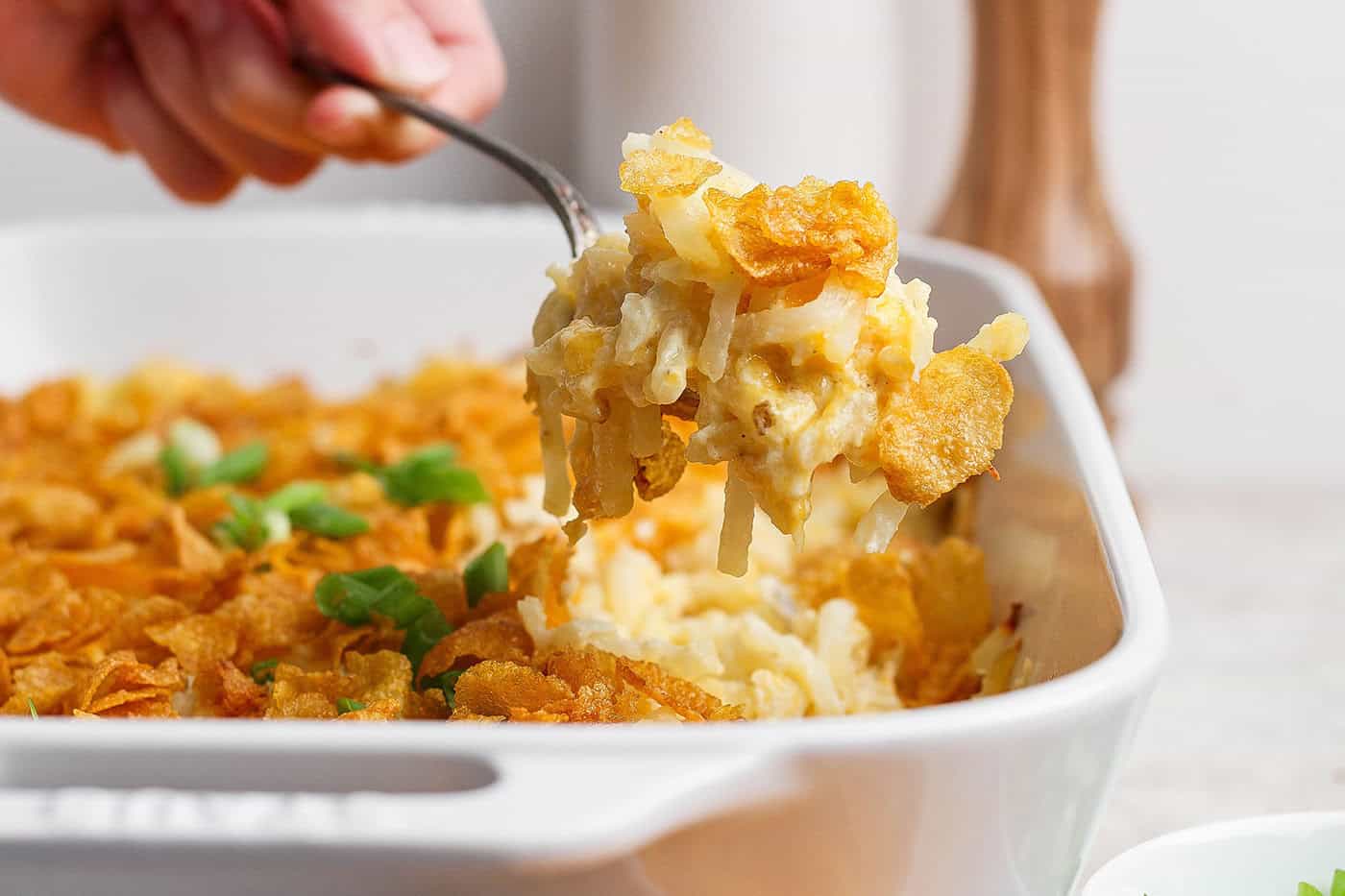 Spoonful of cheesy hashbrown casserole held over dish