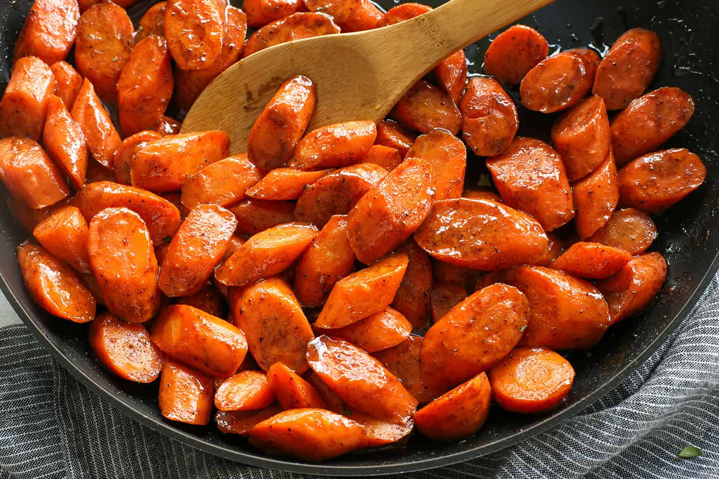 Tossed in a mixture of cinnamon, brown sugar, and honey, these Candied Carrots are perfectly sweet and savory. A quick & easy side dish! A wooden spoon stirring glazed carrots