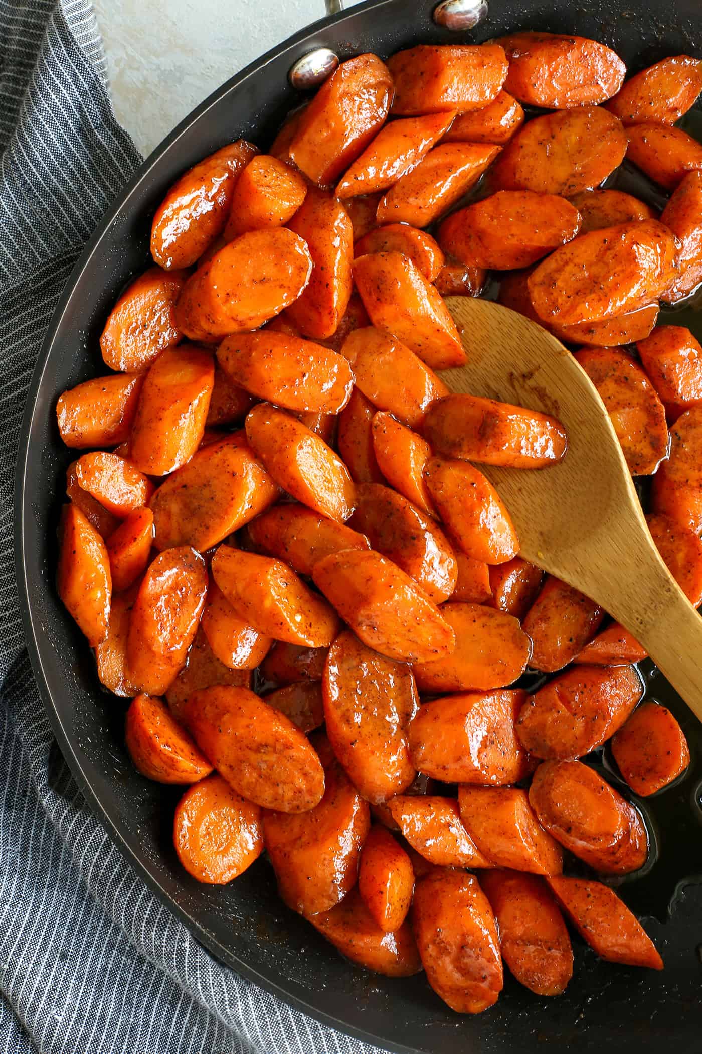 Tossed in a mixture of cinnamon, brown sugar, and honey, these Candied Carrots are perfectly sweet and savory. A quick & easy side dish! Overhead view of a wooden spoon stirring honey glazed carrots