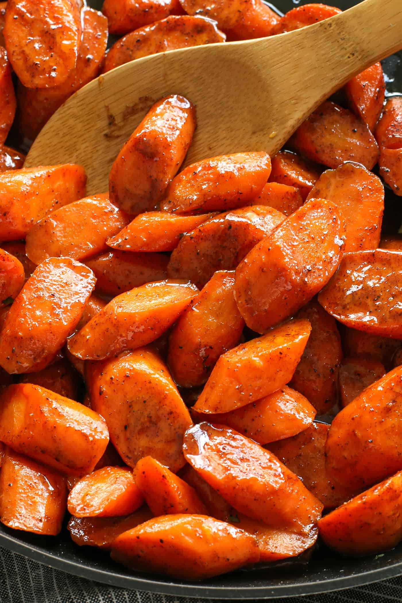 Tossed in a mixture of cinnamon, brown sugar, and honey, these Candied Carrots are perfectly sweet and savory. A quick & easy side dish! Close up of a spoon stirring honey glazed carrots
