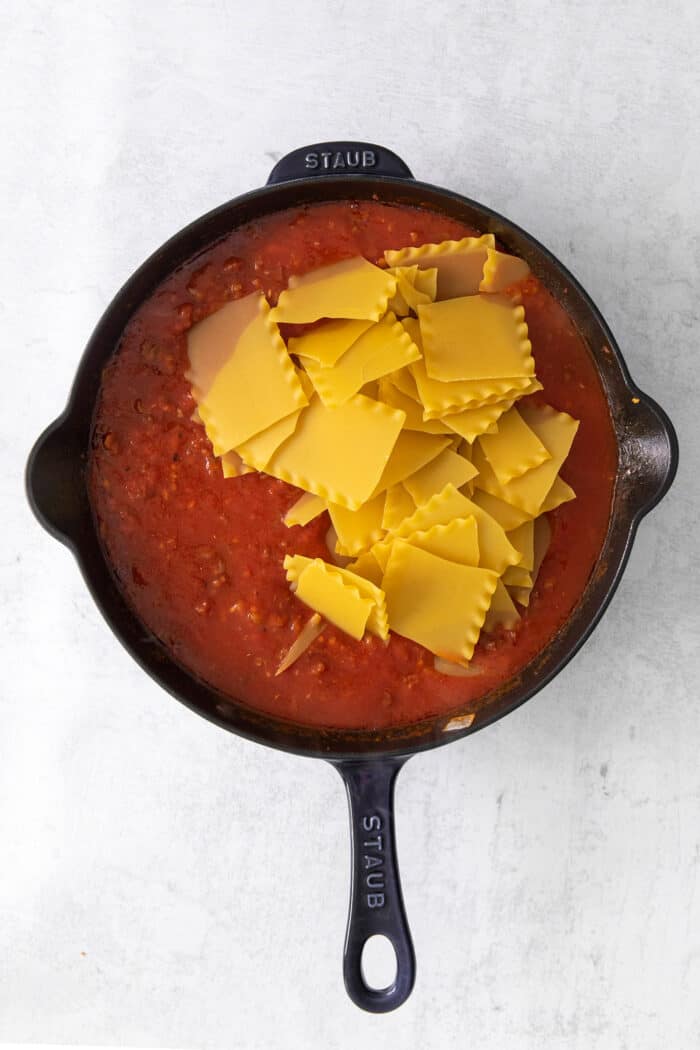 This skillet lasagna recipe has all the classic lasagna ingredients, without the extra dishes and layering! Perfect for weeknight dinners. Broken lasagna noodles and marinara sauce in a cast iron skillet