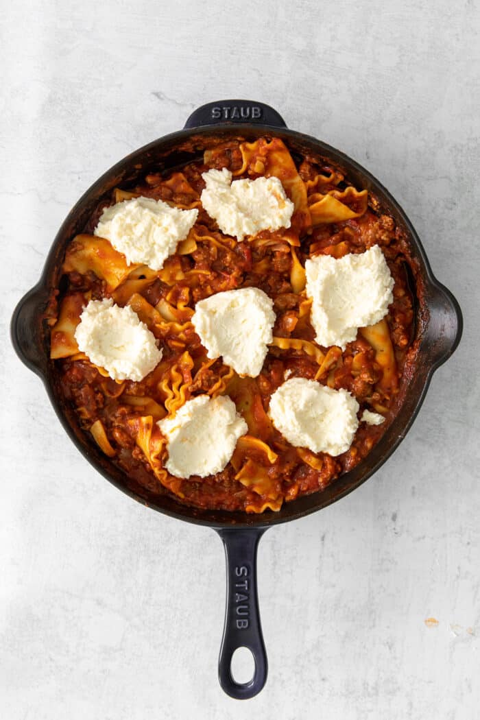 This skillet lasagna recipe has all the classic lasagna ingredients, without the extra dishes and layering! Perfect for weeknight dinners. Dollops of ricotta cheese over lasagna noodles and sauce in a skillet