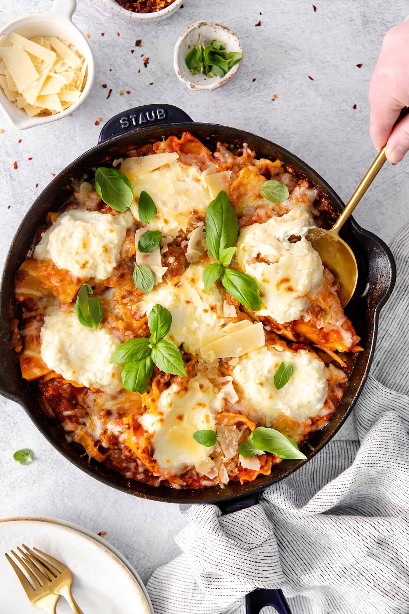 This skillet lasagna recipe has all the classic lasagna ingredients, without the extra dishes and layering! Perfect for weeknight dinners. Overhead view of a hand using a spoon to scoop a serving of lasagna from a skillet