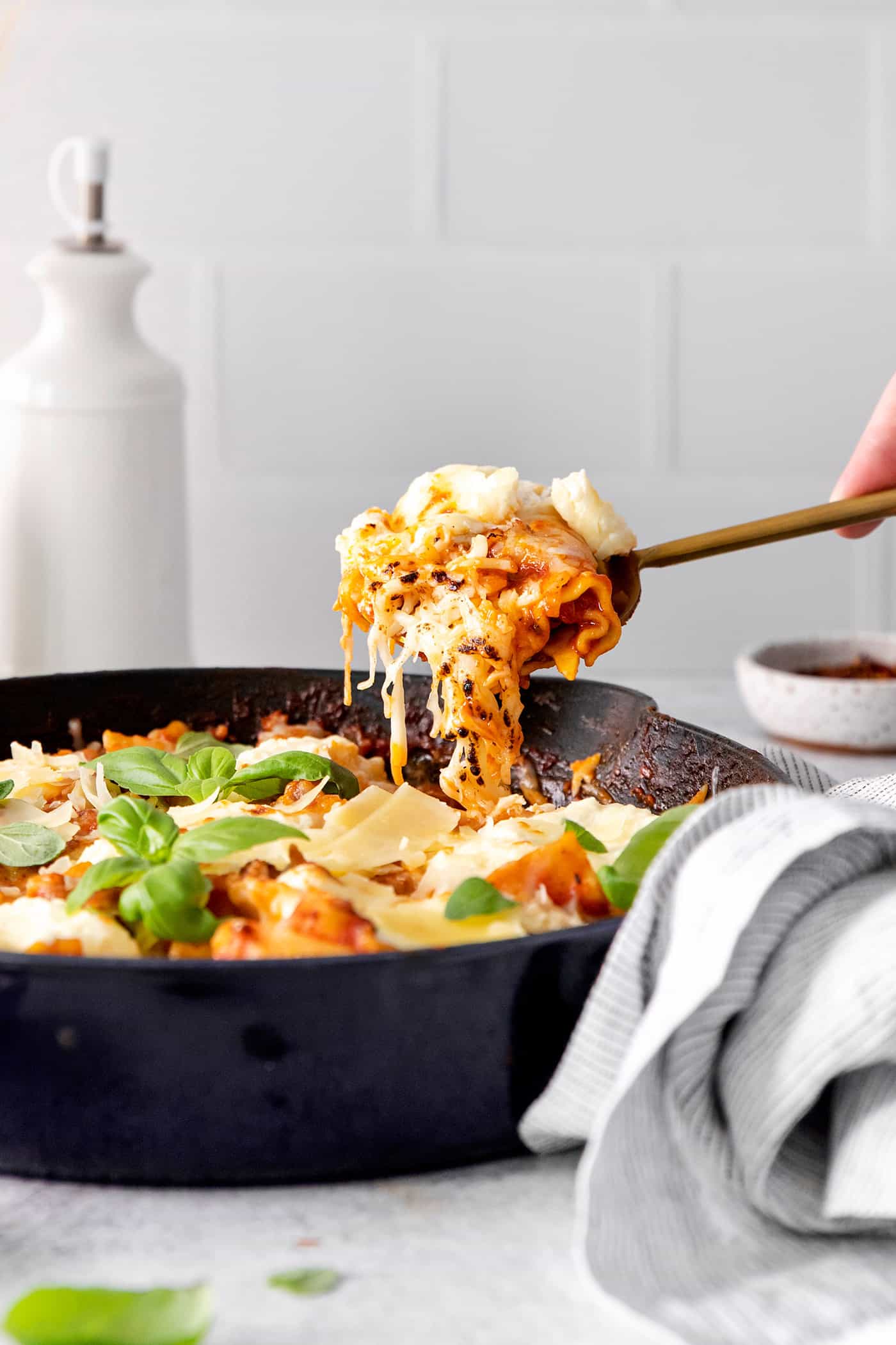 This skillet lasagna recipe has all the classic lasagna ingredients, without the extra dishes and layering! Perfect for weeknight dinners. A spoon scooping a serving of cheesy lasagna from a skillet.