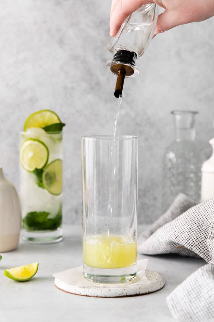 Simple syrup being added to a glass with lime juice