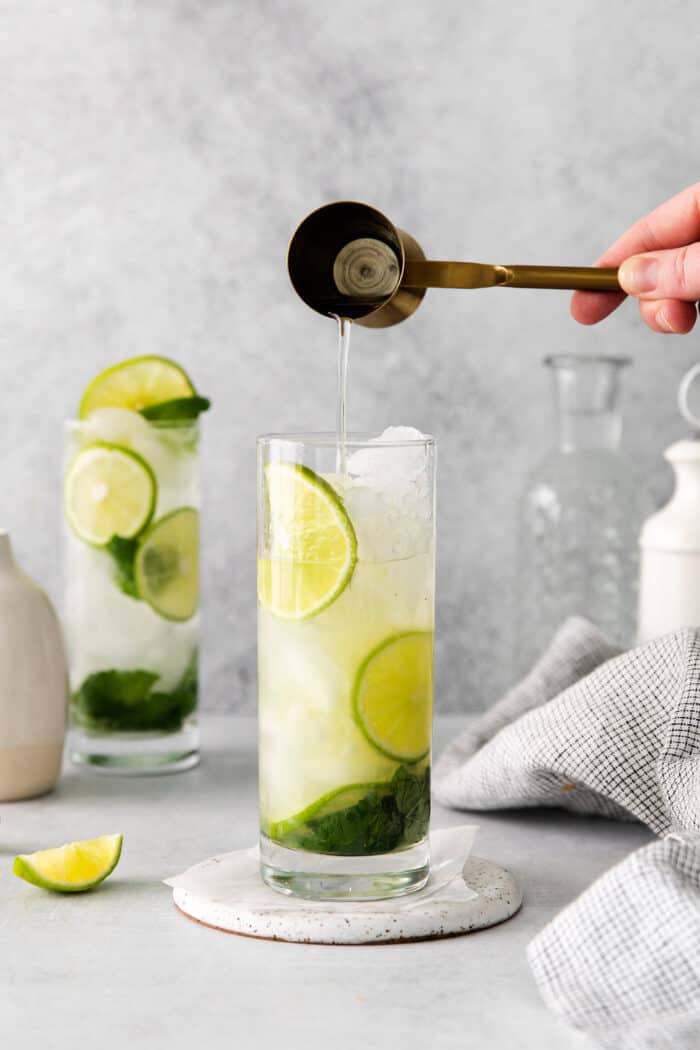 Tequila being added to a mojito in a tall glass