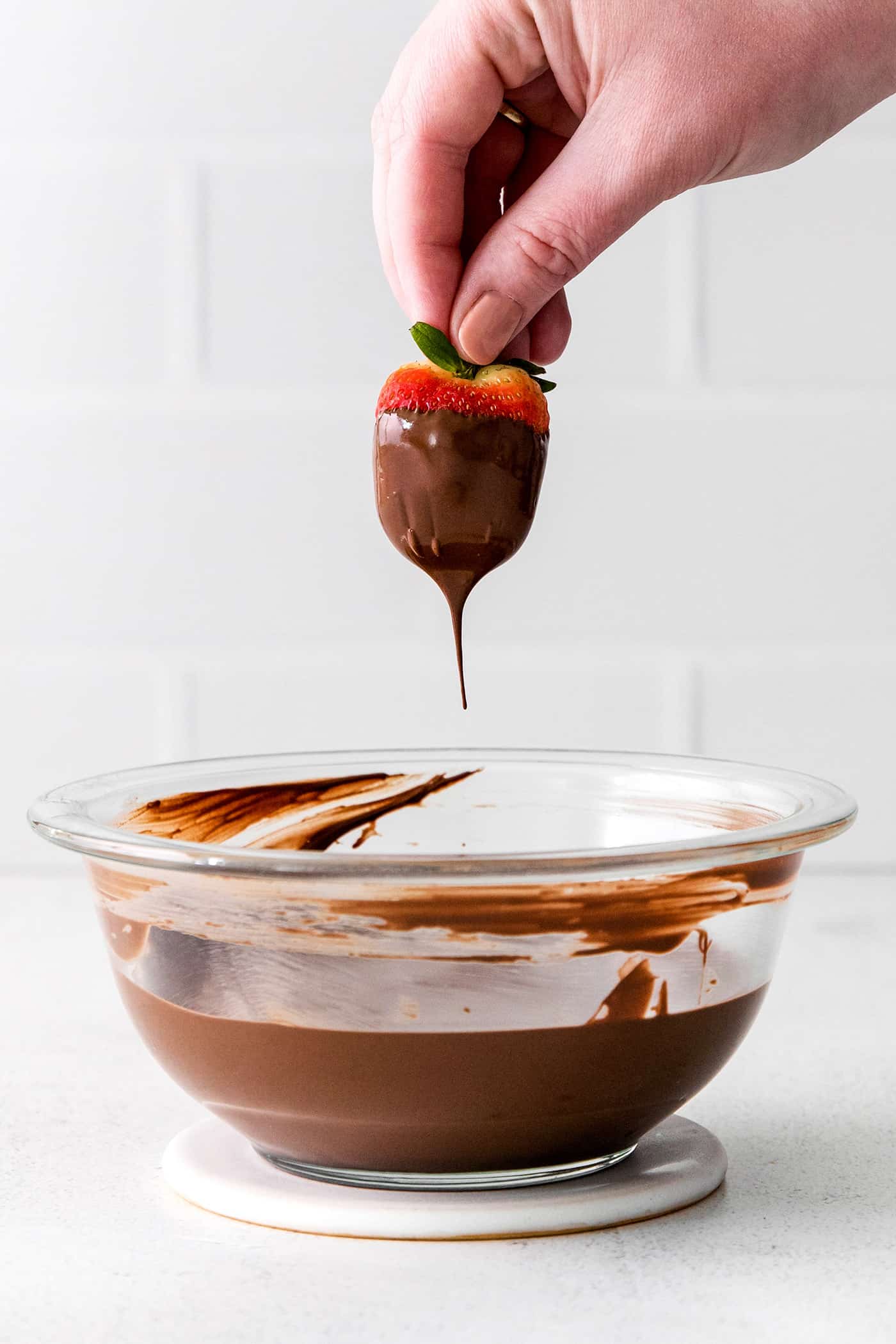 These Chocolate Covered Strawberries may look fancy and elegant, but are actually a quick and easy treat to make, with just 3 ingredients! A hand dipping a strawberry into melted chocolate