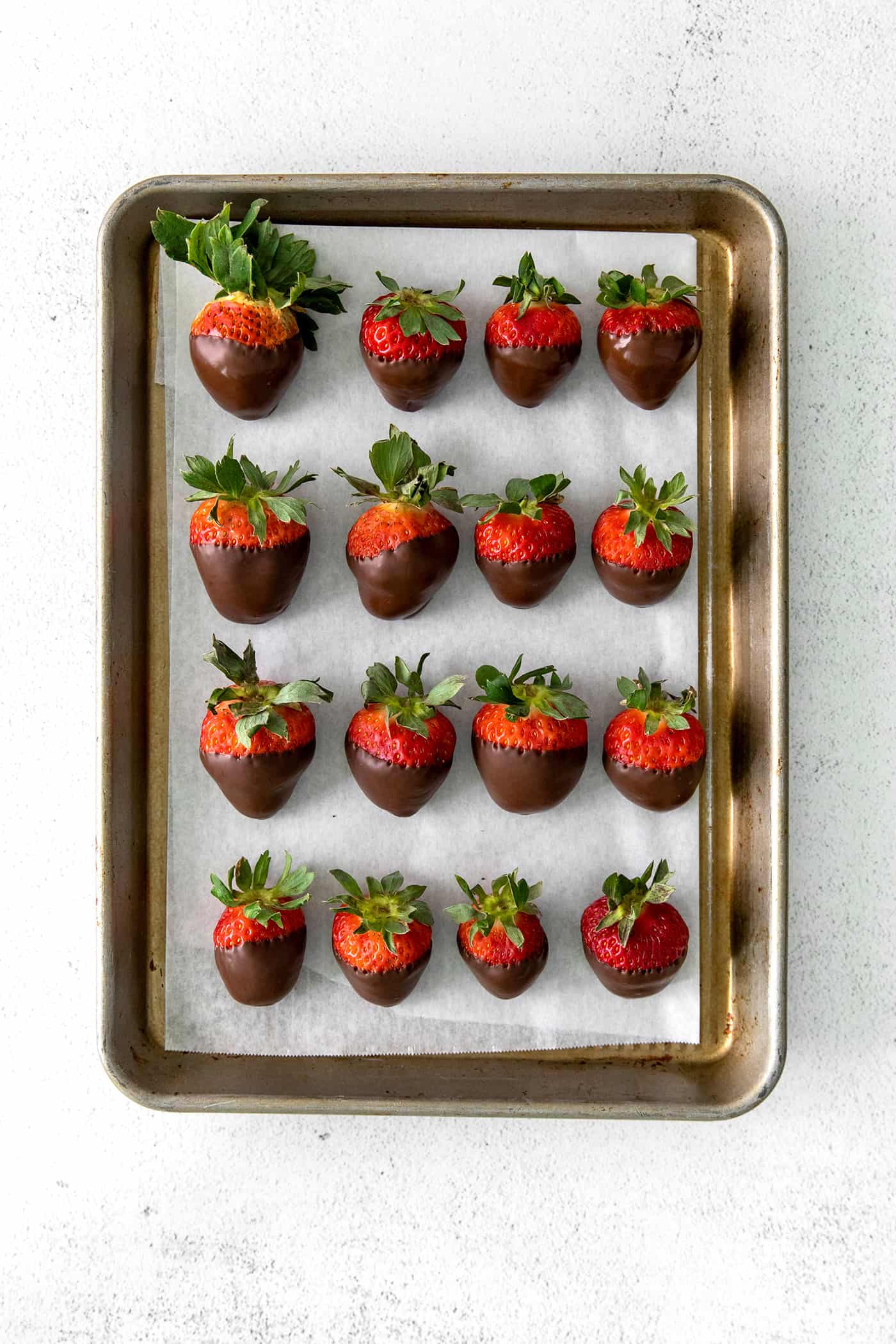 These Chocolate Covered Strawberries may look fancy and elegant, but are actually a quick and easy treat to make, with just 3 ingredients! Overhead view of a baking sheet of chocolate covered strawberries