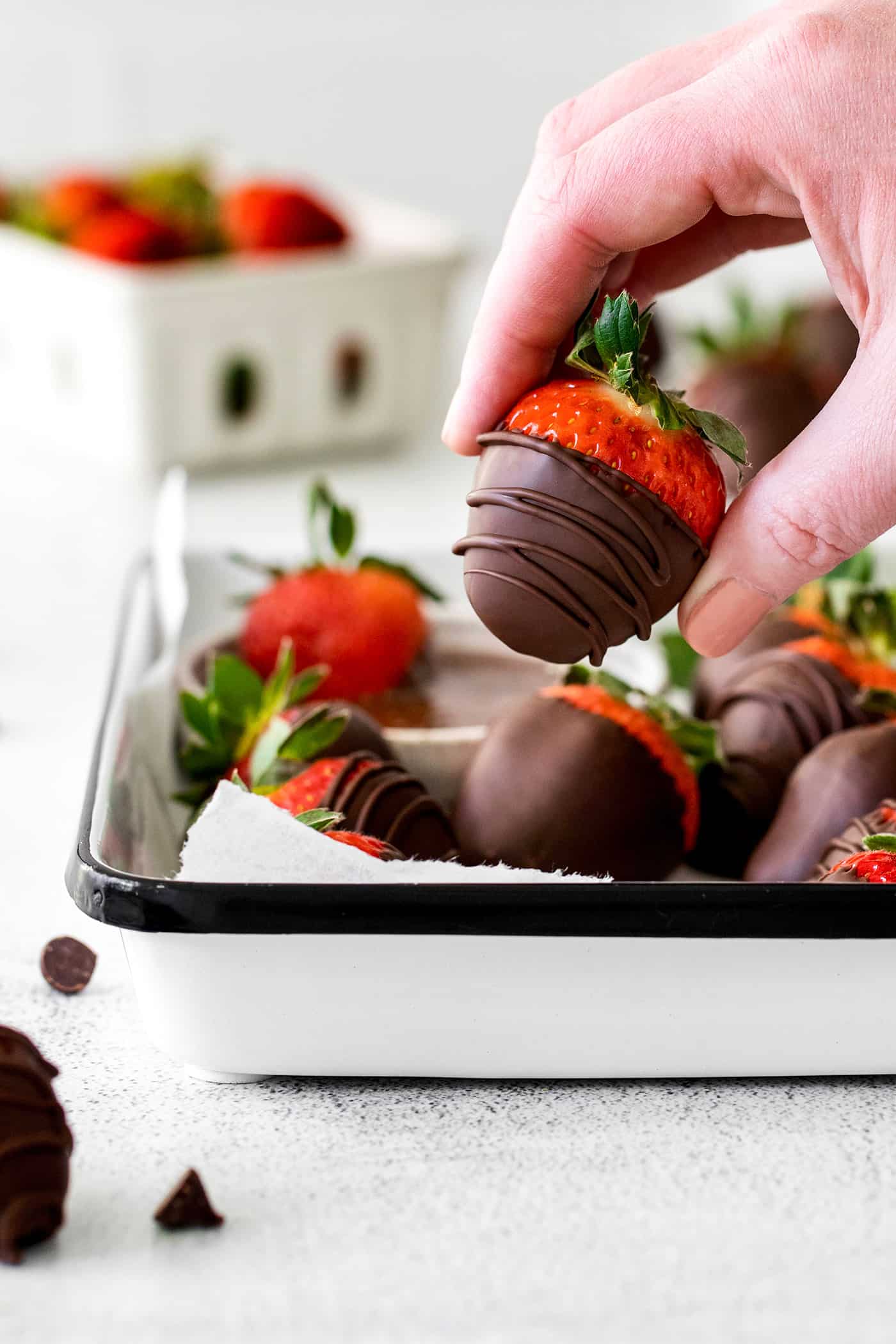 These Chocolate Covered Strawberries may look fancy and elegant, but are actually a quick and easy treat to make, with just 3 ingredients! A hand holding a chocolate covered strawberry