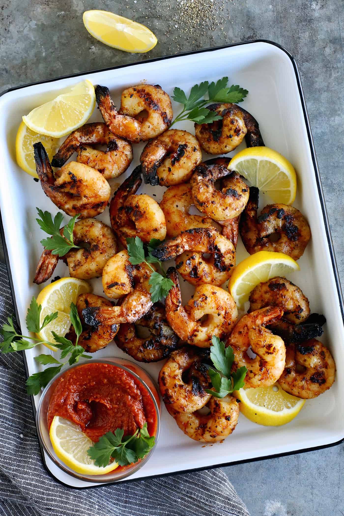 Tossed with olive oil and a few spices, this easy shrimp cocktail is perfectly flavored and grilled until just charred. So good! Grilled shrimp cocktail on a white serving plate.
