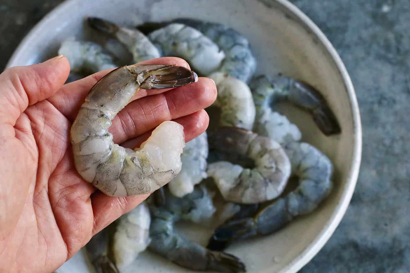 Tossed with olive oil and a few spices, this easy shrimp cocktail is perfectly flavored and grilled until just charred. So good! A hand holding a jumbo shrimp.