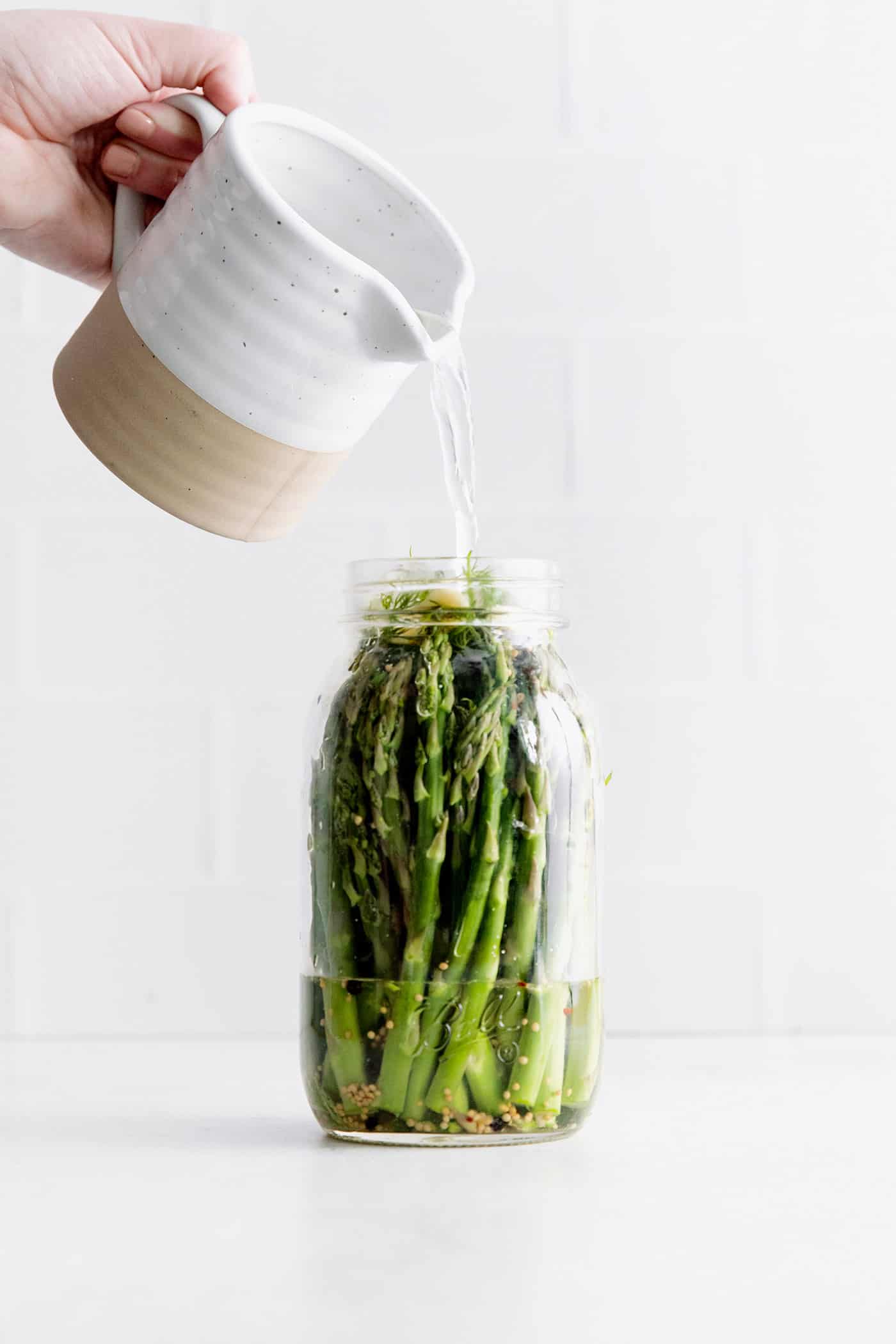With a simple pickling brine and a few spices, these Quick Pickled Asparagus has a tangy, robust flavor with just a bit of heat. Pickling brine being poured over a jar of asparagus