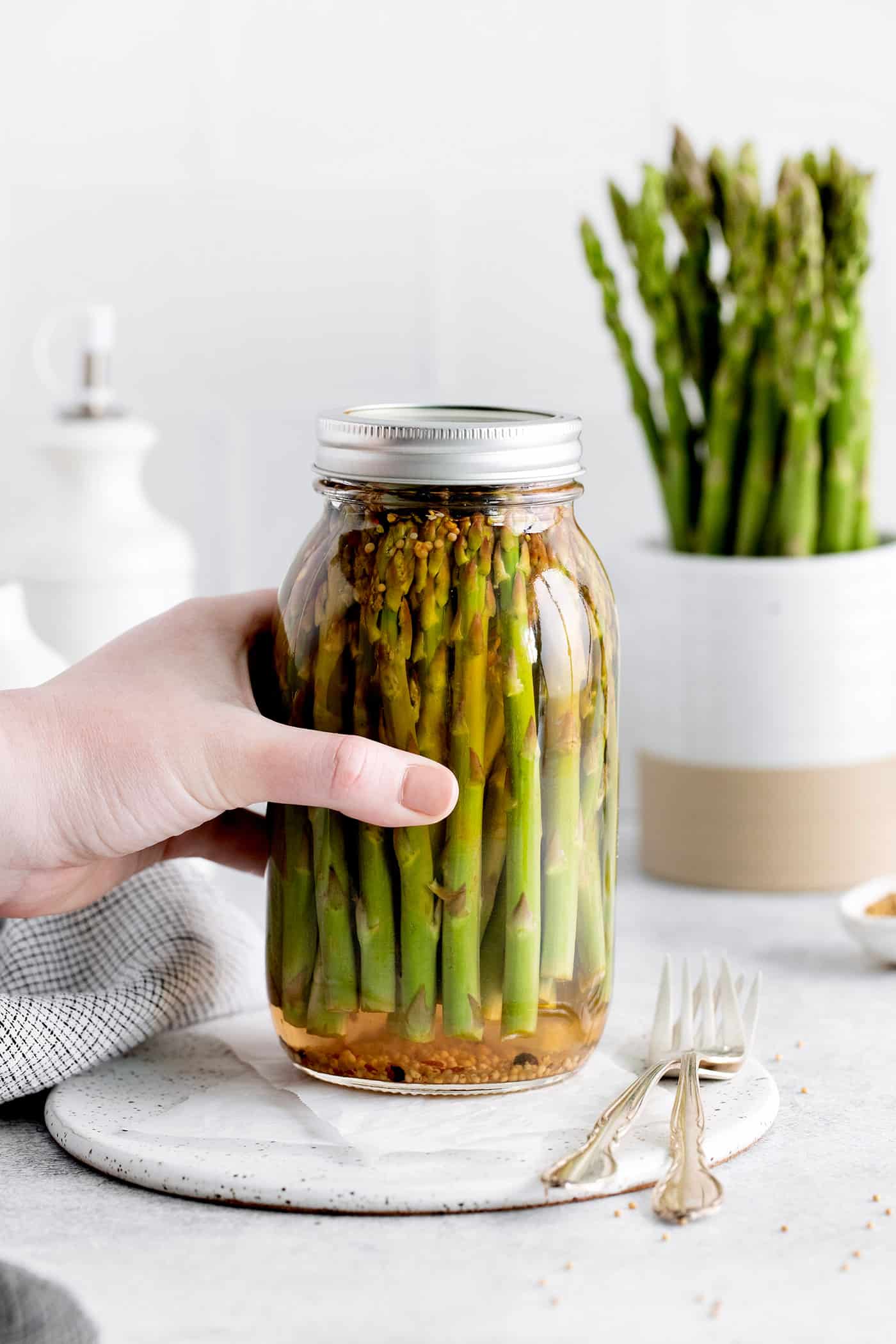 With a simple pickling brine and a few spices, these Quick Pickled Asparagus has a tangy, robust flavor with just a bit of heat. A hand grabbing a jar of asparagus
