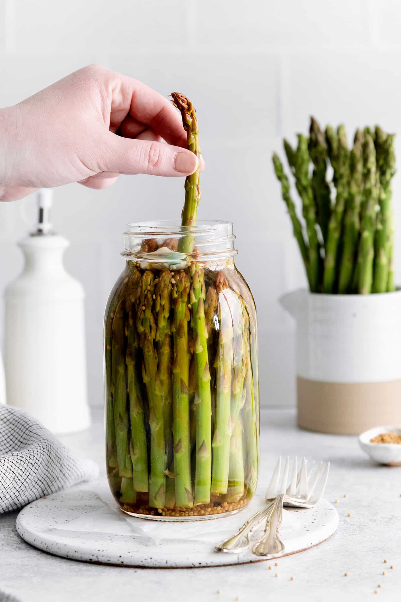 With a simple pickling brine and a few spices, these Quick Pickled Asparagus has a tangy, robust flavor with just a bit of heat. A hand pulling an asparagus from a jar