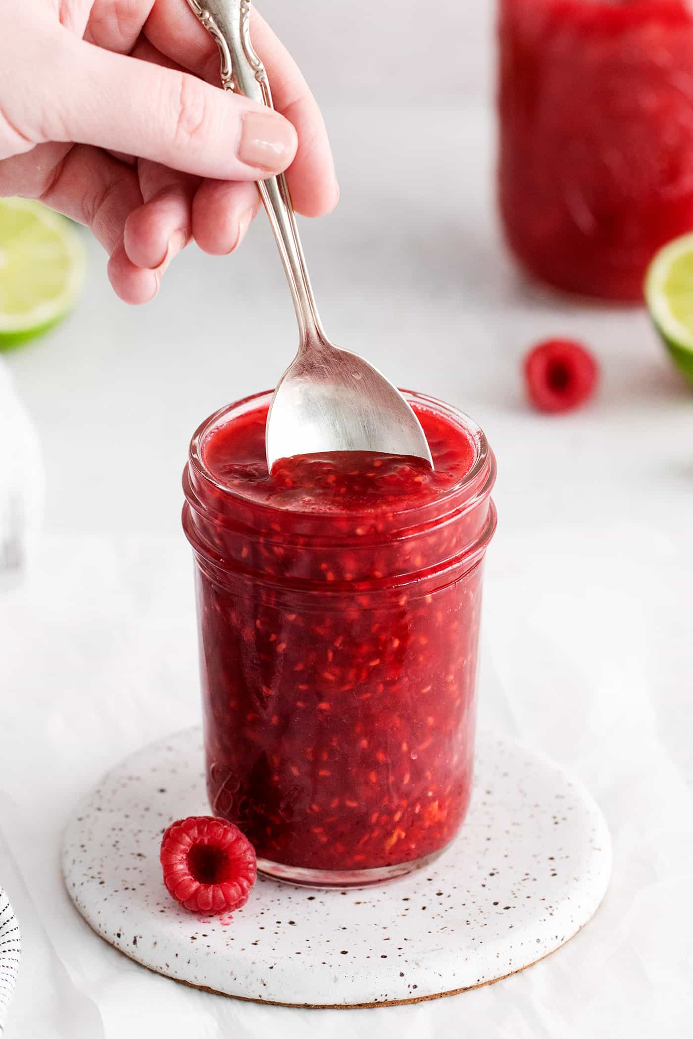 Sweet, bright, and intensely fruity this Raspberry Sauce makes a great topping for angel food cake, cheesecake, ice cream, and more. A spoon diving into a jar of raspberry sauce