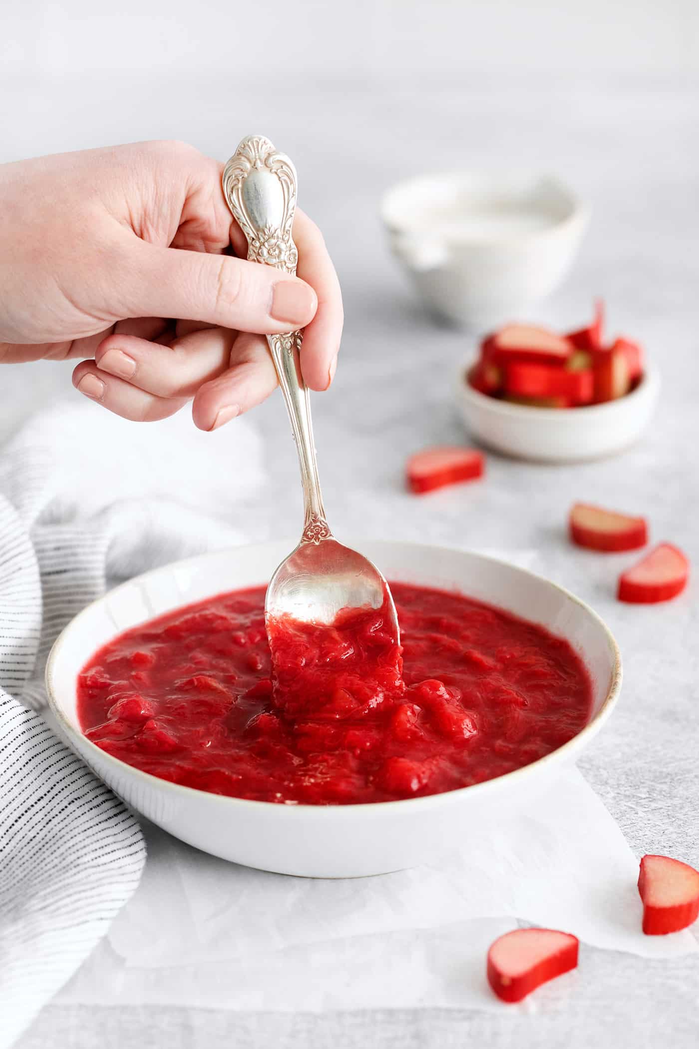 With just 3 ingredients - sugar, water, and rhubarb - you can make this sweet and tart Rhubarb Sauce. Use on ice cream, cake & more. A spoon stirring a bowl of rhubarb sauce