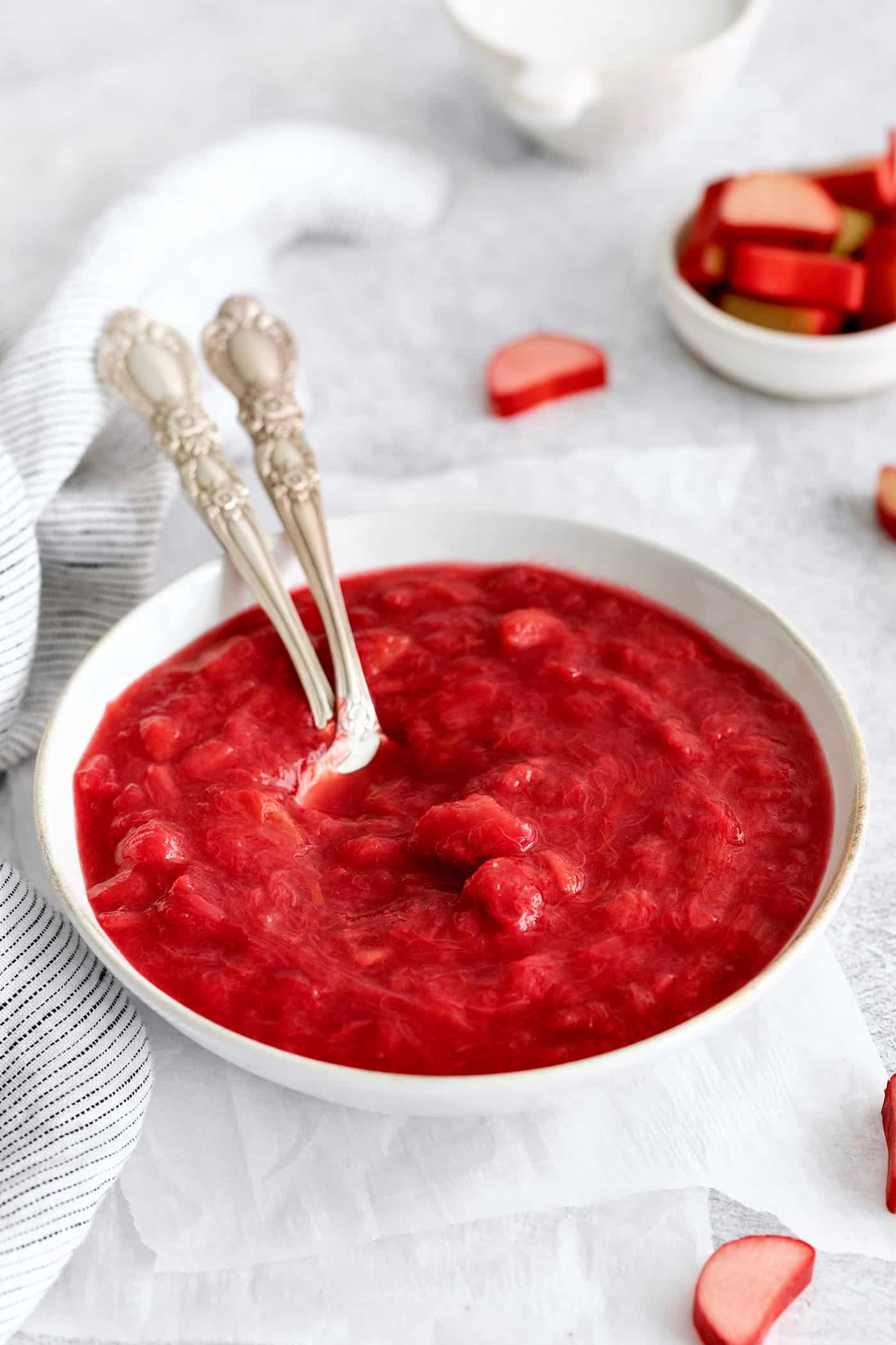 With just 3 ingredients - sugar, water, and rhubarb - you can make this sweet and tart Rhubarb Sauce. Use on ice cream, cake & more. Two spoons in a bowl of rhubarb sauce