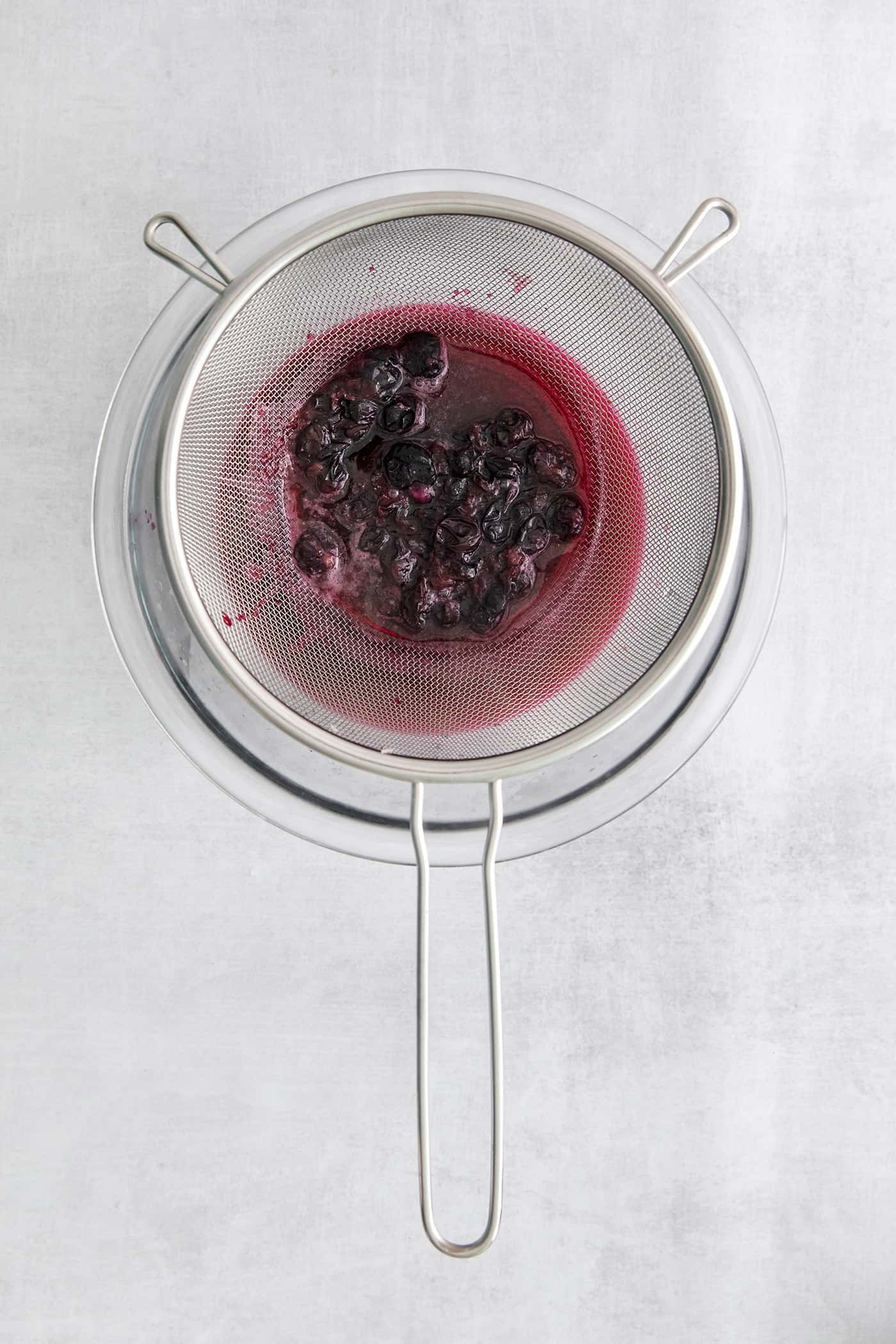 Made with flavored simple syrup, this Blueberry Margarita is just the fruity cocktail for summer. Sweet but tart and super refreshing! Blueberry syrup being pushed through a strainer