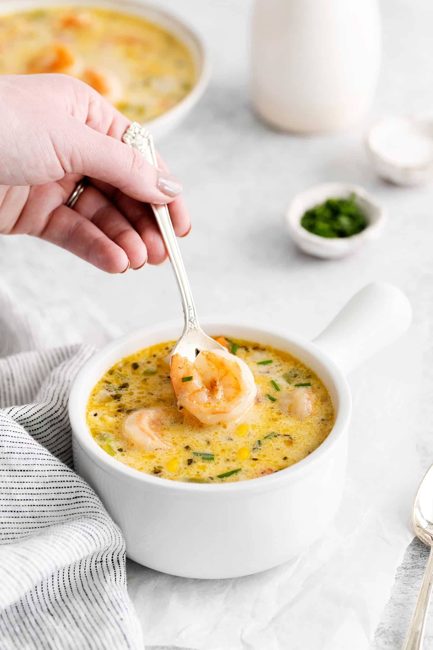 This shrimp and corn chowder has a light, creamy broth and is filled with sautéed vegetables, tender shrimp, and fresh sweet corn. A spoon lifting a shrimp from a bowl of shrimp corn chowder