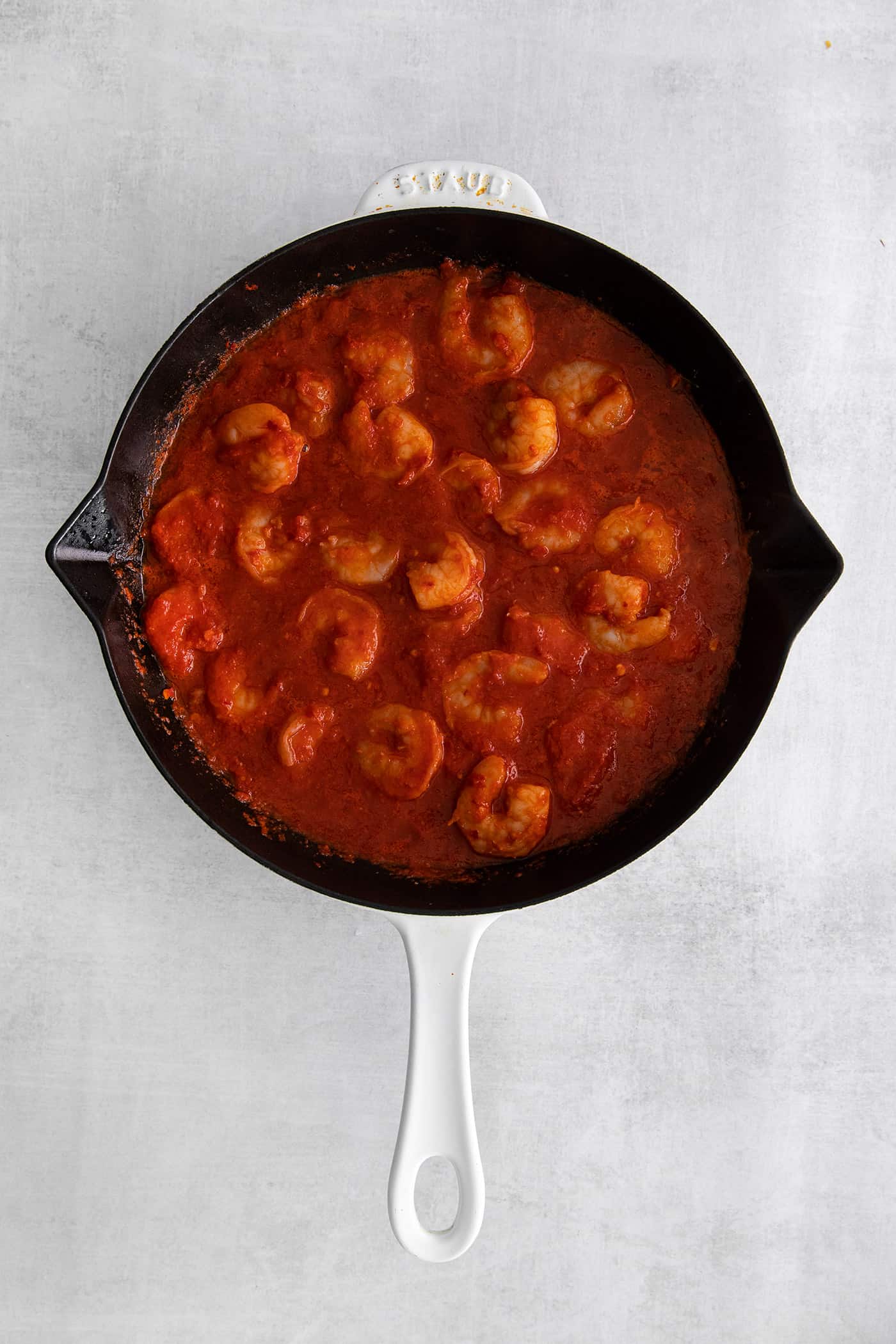 Camarones a la Diabla is a classic Mexican seafood dish that features fresh shrimp, dried chiles, and ripe tomatoes. Ready in 30 minutes! Overhead view of shrimp in a cast iron skillet with red sauce