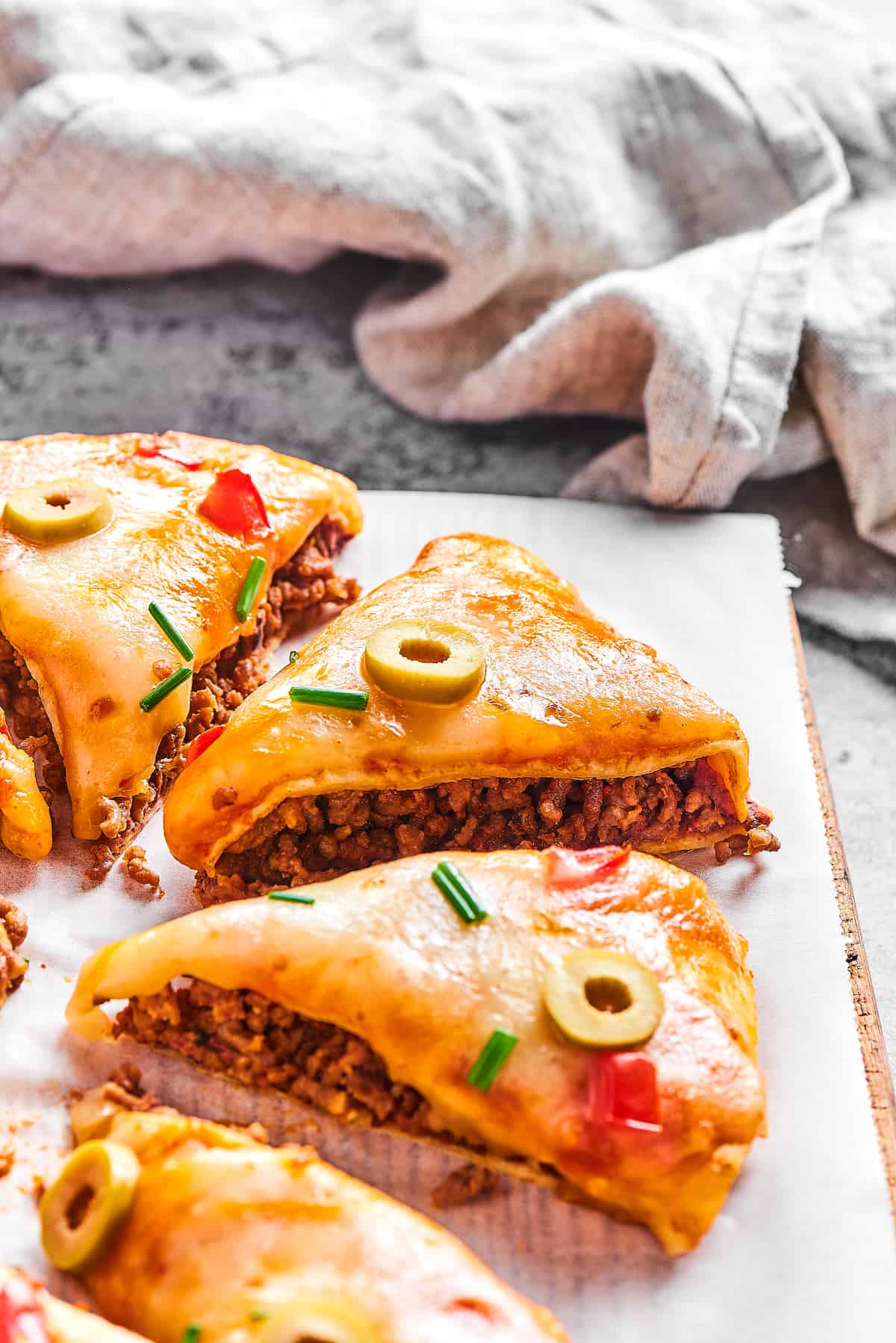 Made with taco meat, refried beans, and enchilada sauce layers with tortillas and cheese, Mexican Pizza is easy & tasty. Close-up of triangles of Mexican pizza topped with sliced green olives
