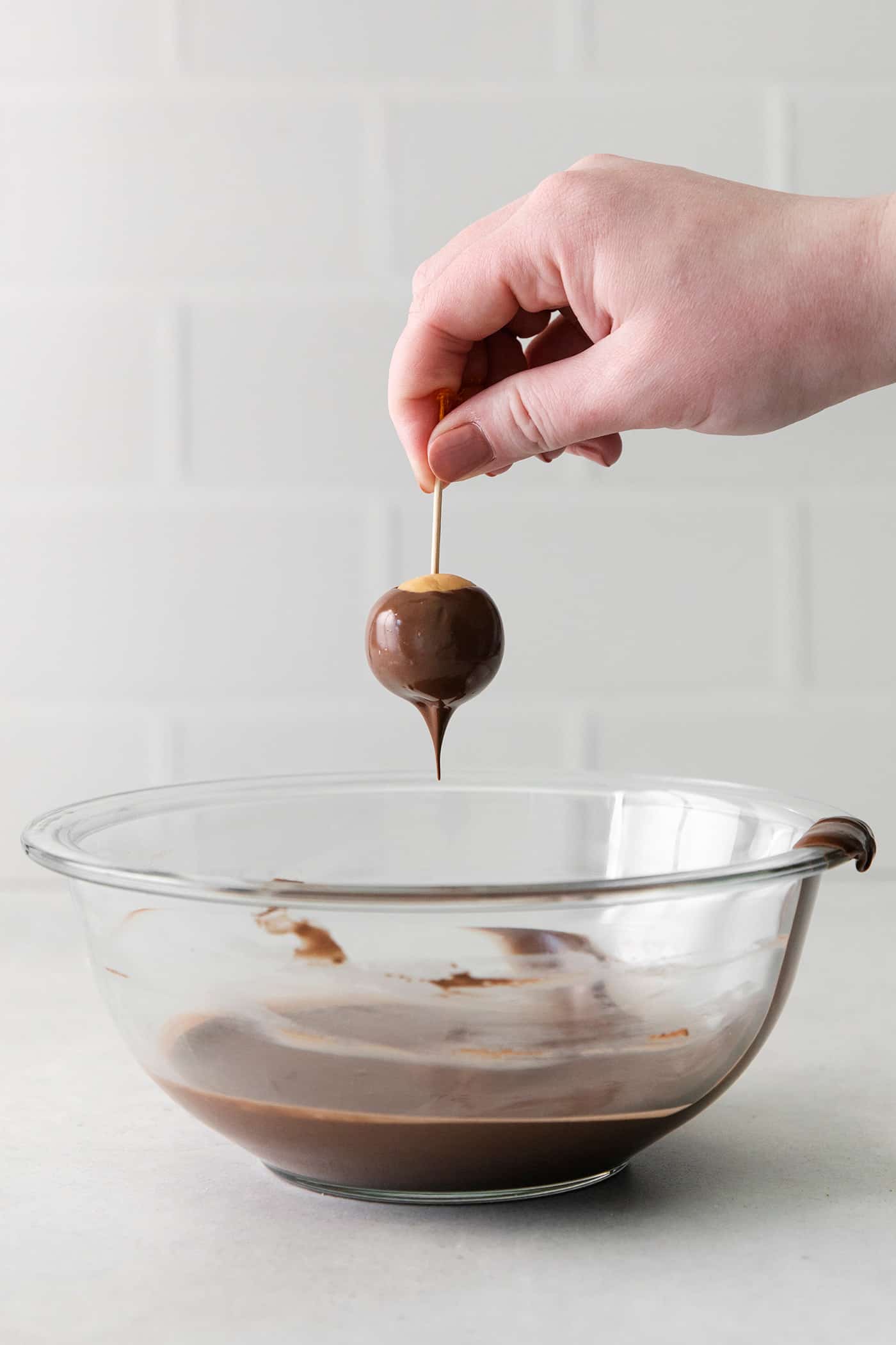 These Homemade Buckeyes feature creamy peanut butter balls dipped in rich, smooth semi-sweet chocolate. Just 7 ingredients! A hand reaching for a buckeye