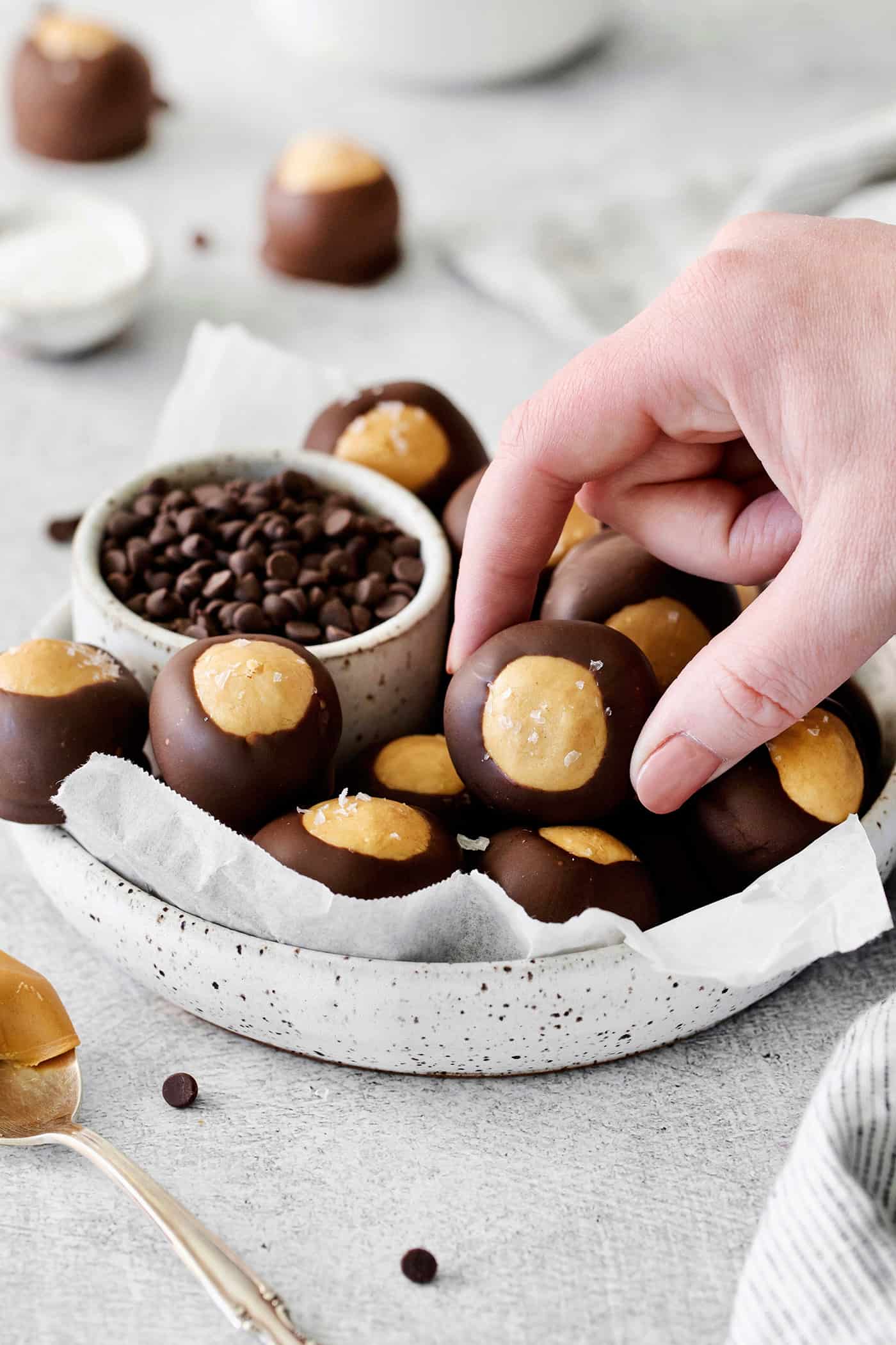 These Homemade Buckeyes feature creamy peanut butter balls dipped in rich, smooth semi-sweet chocolate. Just 7 ingredients! A hand grabbing a buckeye candy