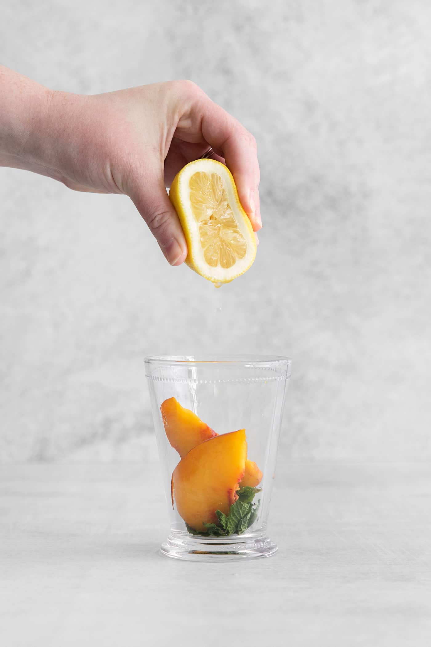 This Peach Mint Julep is bright, fresh, and fruity, with a hint of spice from fresh ginger. The perfect summer cocktail! Lemon juice being squeezed into a cocktail glass with peach and mint