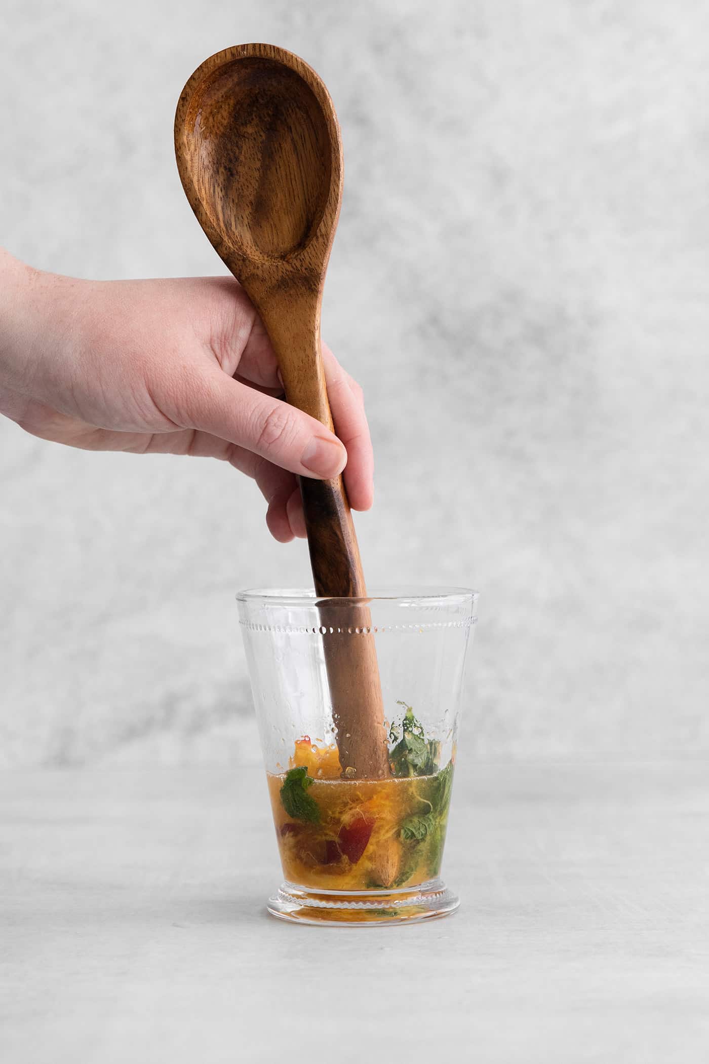 This Peach Mint Julep is bright, fresh, and fruity, with a hint of spice from fresh ginger. The perfect summer cocktail! The end of a wooden spoon muddling peaches and mint in a cocktail glass