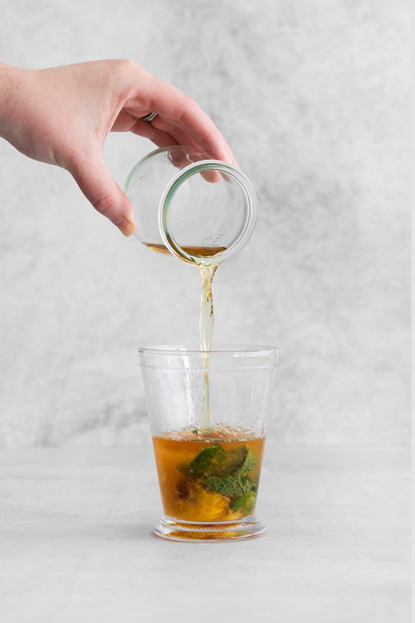 This Peach Mint Julep is bright, fresh, and fruity, with a hint of spice from fresh ginger. The perfect summer cocktail! Bourbon being poured into a glass with muddled peaches and mint
