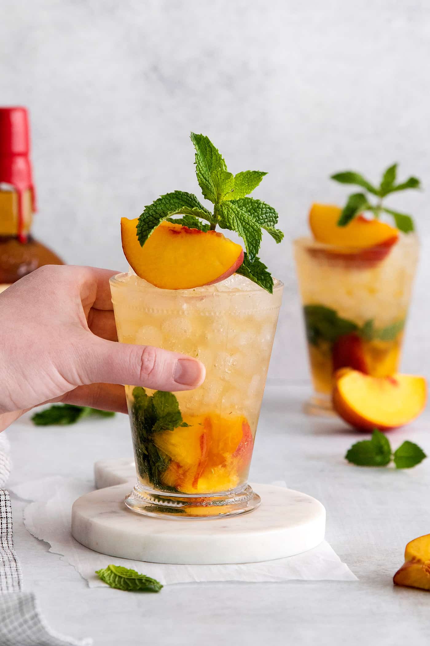 This Peach Mint Julep is bright, fresh, and fruity, with a hint of spice from fresh ginger. The perfect summer cocktail! A hand grabbing a peach mint julep cocktail