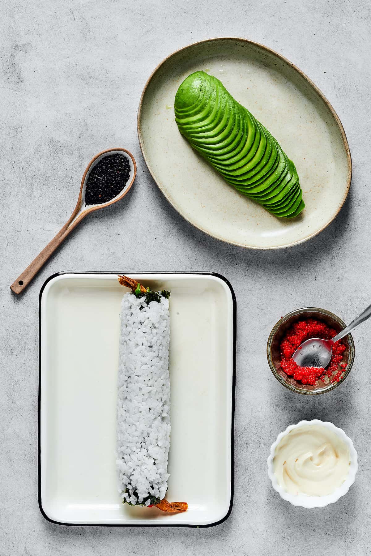 This dragon roll features tempura shrimp, cucumber, tobiko, and avocado wrapped in nori and rice. It's easy to make and such a crowd-pleaser! A sushi roll and a plate of avocado slices.