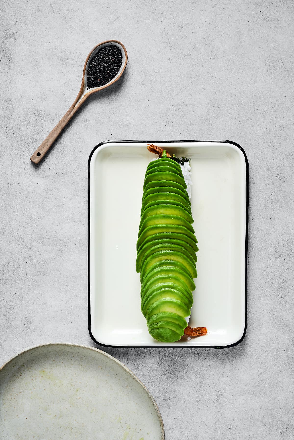 This dragon roll features tempura shrimp, cucumber, tobiko, and avocado wrapped in nori and rice. It's easy to make and such a crowd-pleaser! Slices of avocado on a sushi roll.