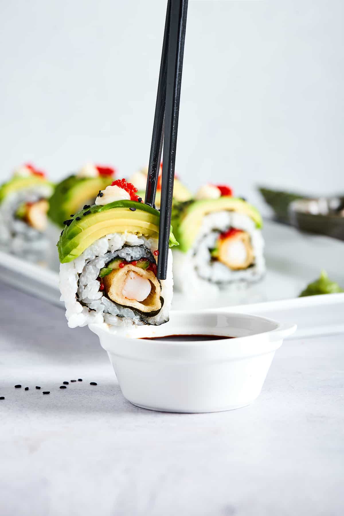 This dragon roll features tempura shrimp, cucumber, tobiko, and avocado wrapped in nori and rice. It's easy to make and such a crowd-pleaser! Chop sticks with a piece of dragon roll over a dish of soy sauce.