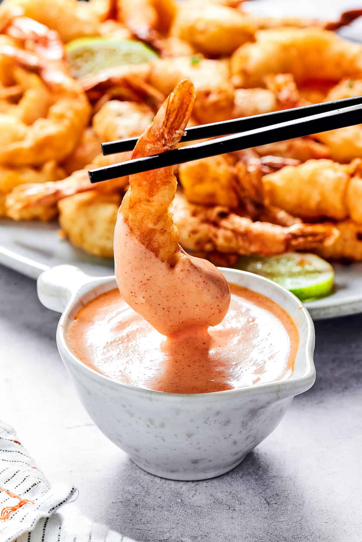 This easy shrimp tempura recipe features juicy, tender shrimp dipped in a light tempura batter. It's then deep-fried until perfectly crispy! Chopsticks holding a fried shrimp in sauce