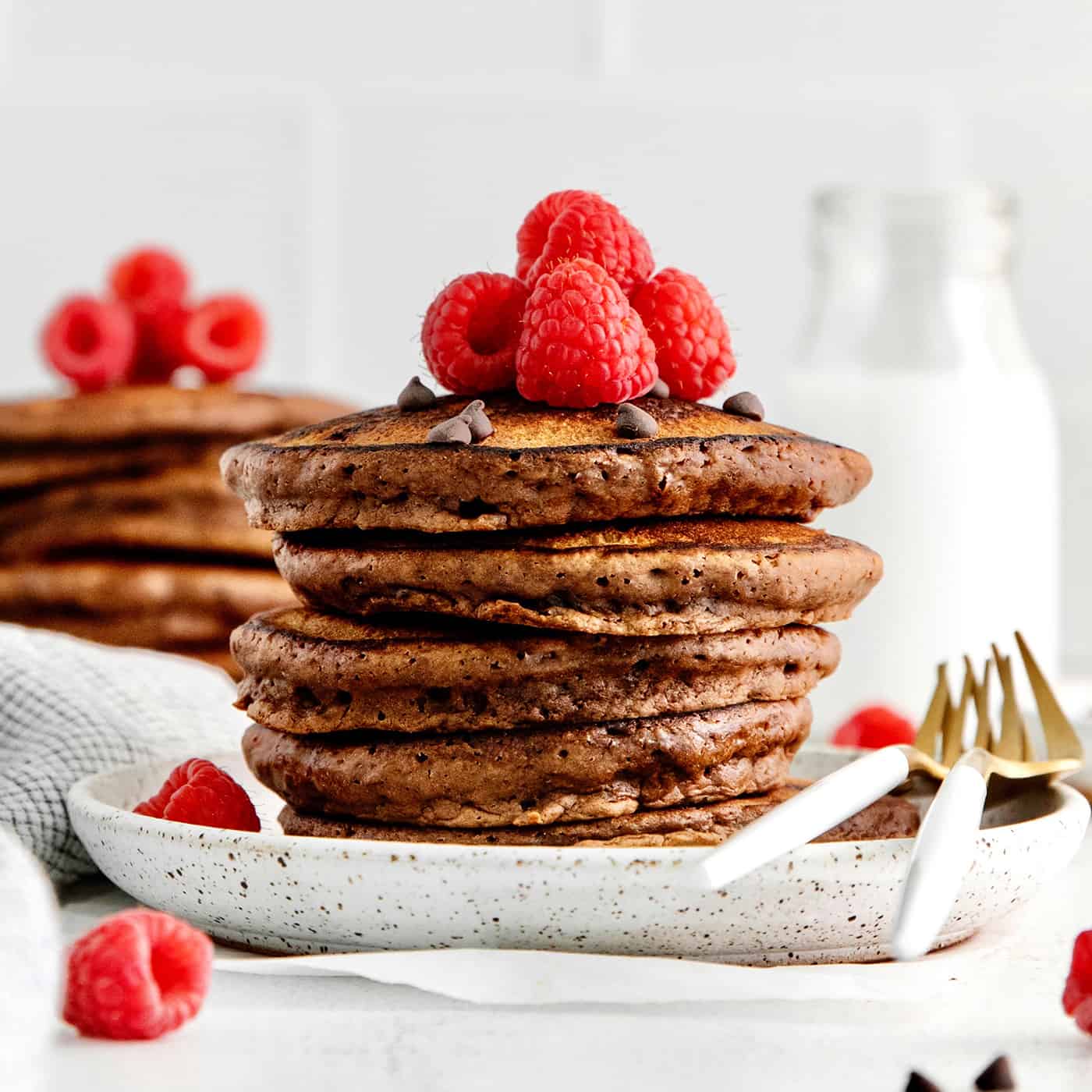 Fluffy, fudgy chocolate pancakes are rich in flavor with pockets of melty chocolate chips throughout. The real chocolate lover's breakfast! A stack of double chocolate pancakes topped with raspberries