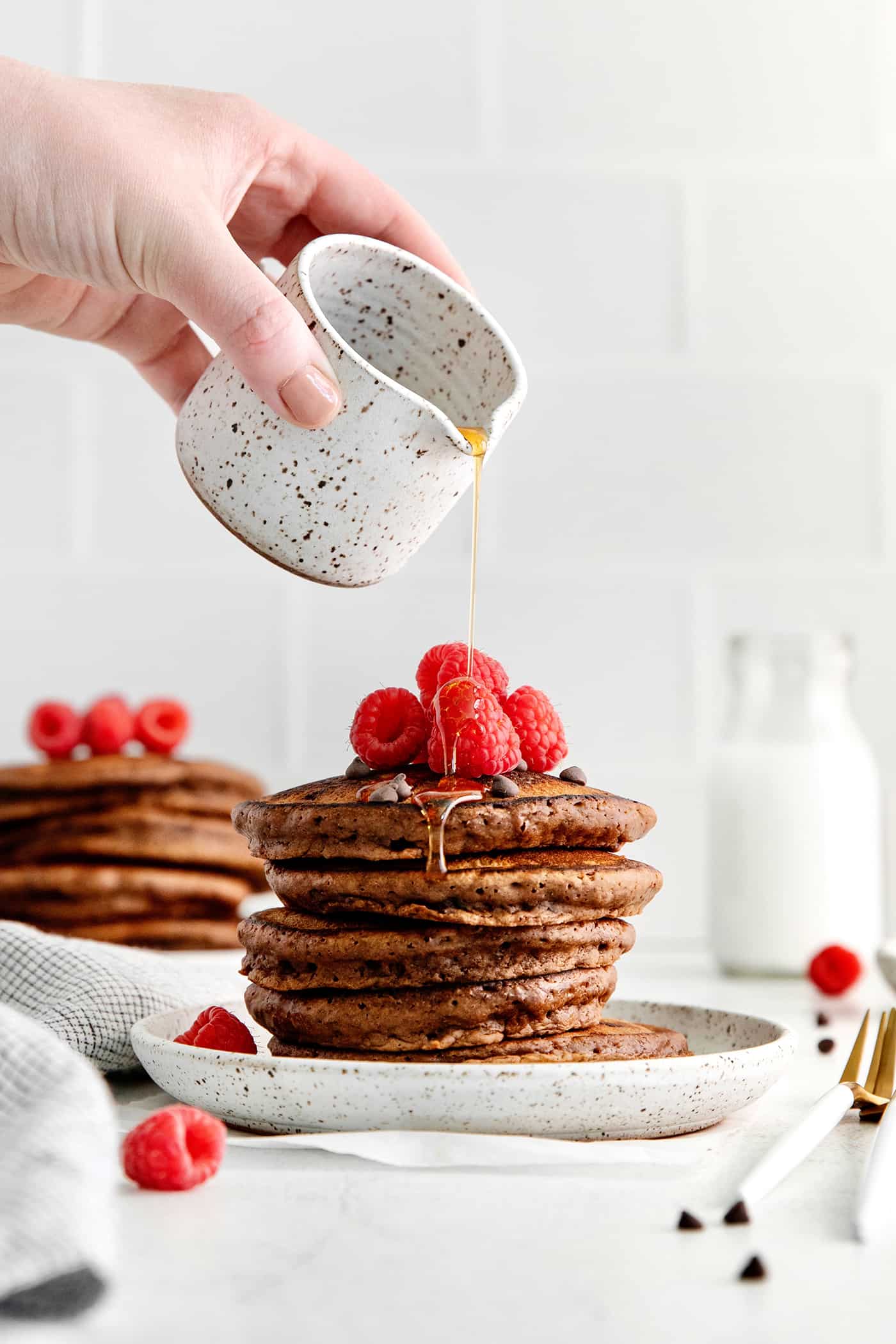 Fluffy, fudgy chocolate pancakes are rich in flavor with pockets of melty chocolate chips throughout. The real chocolate lover's breakfast! A hand pouring syrup over a stack of chocolate pancakes