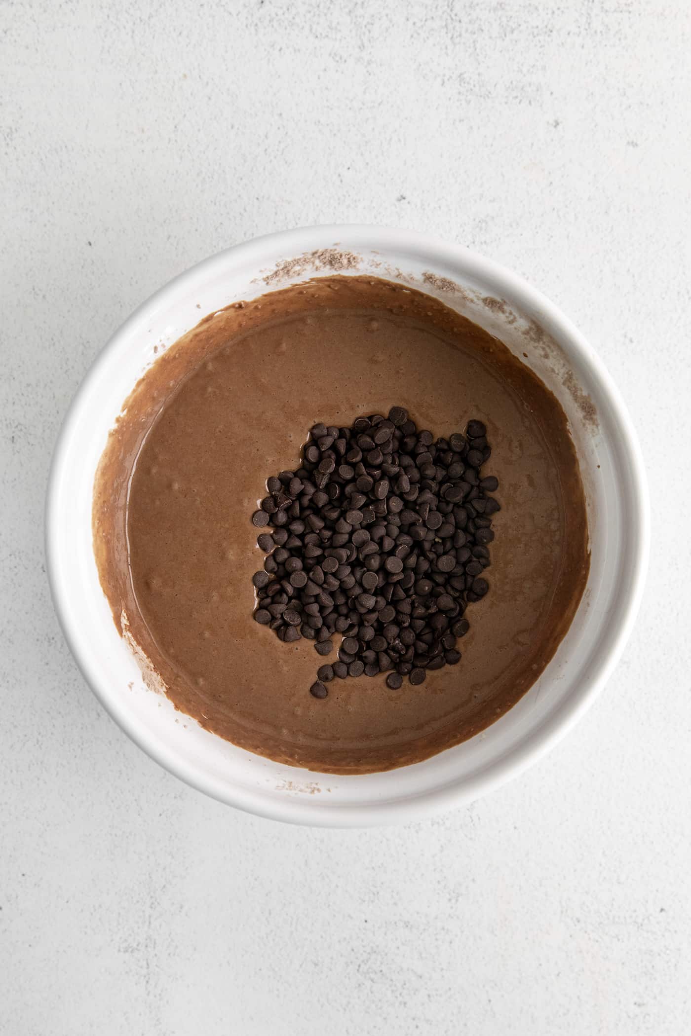 Fluffy, fudgy chocolate pancakes are rich in flavor with pockets of melty chocolate chips throughout. The real chocolate lover's breakfast! Chocolate pancake batter in a white bowl