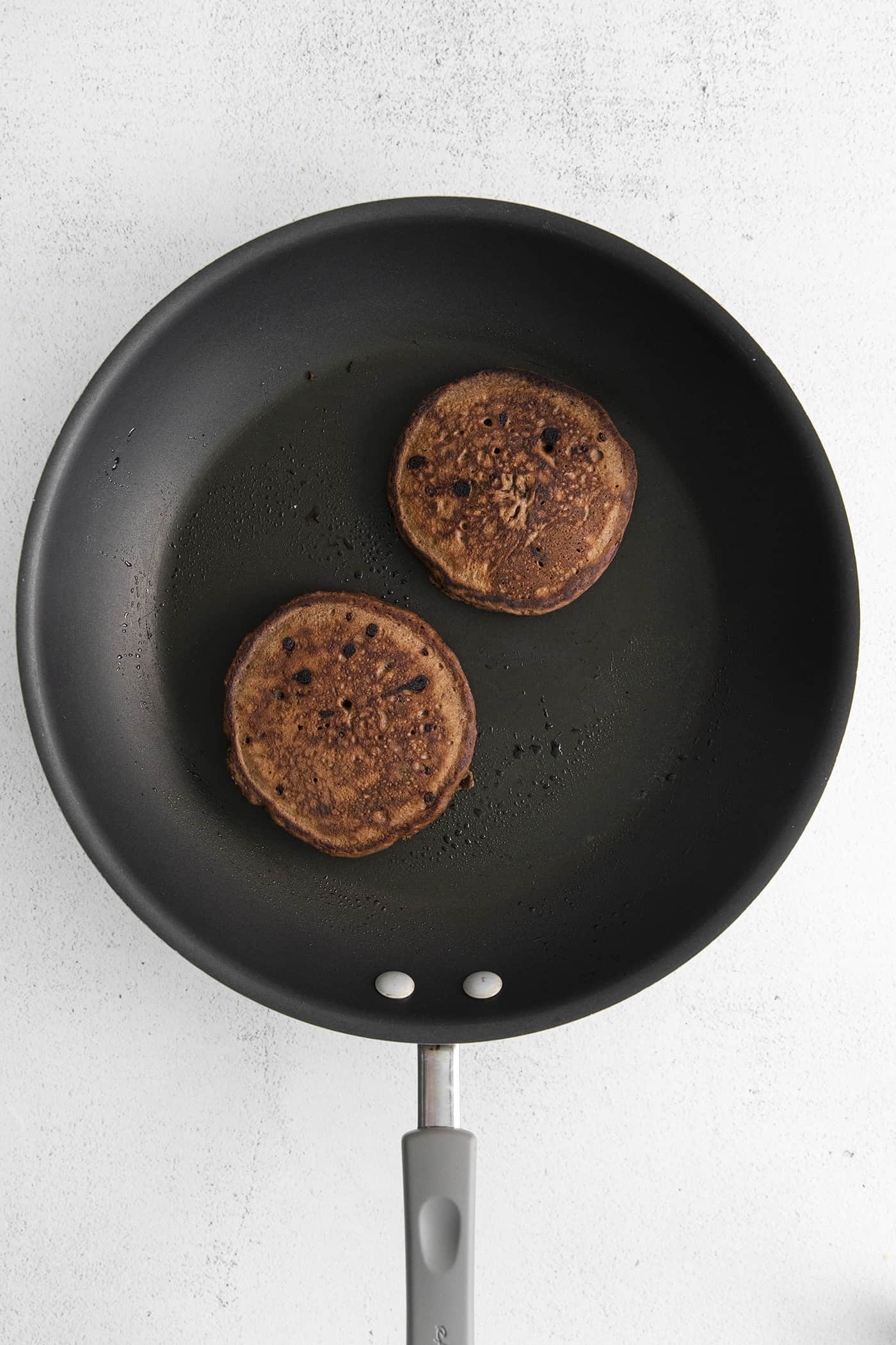 Fluffy, fudgy chocolate pancakes are rich in flavor with pockets of melty chocolate chips throughout. The real chocolate lover's breakfast! Two chocolate pancakes in a skillet