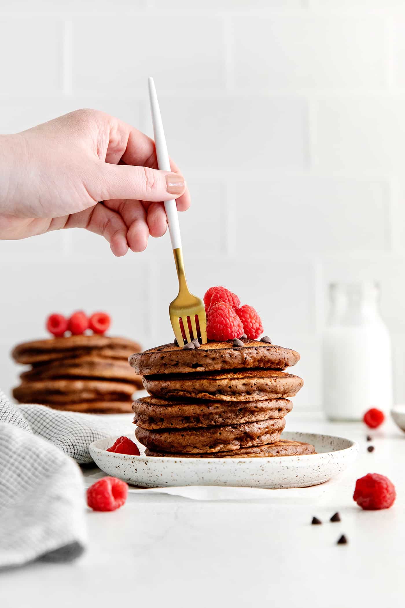 Fluffy, fudgy chocolate pancakes are rich in flavor with pockets of melty chocolate chips throughout. The real chocolate lover's breakfast! A fork diving into a stack of chocolate pancakes
