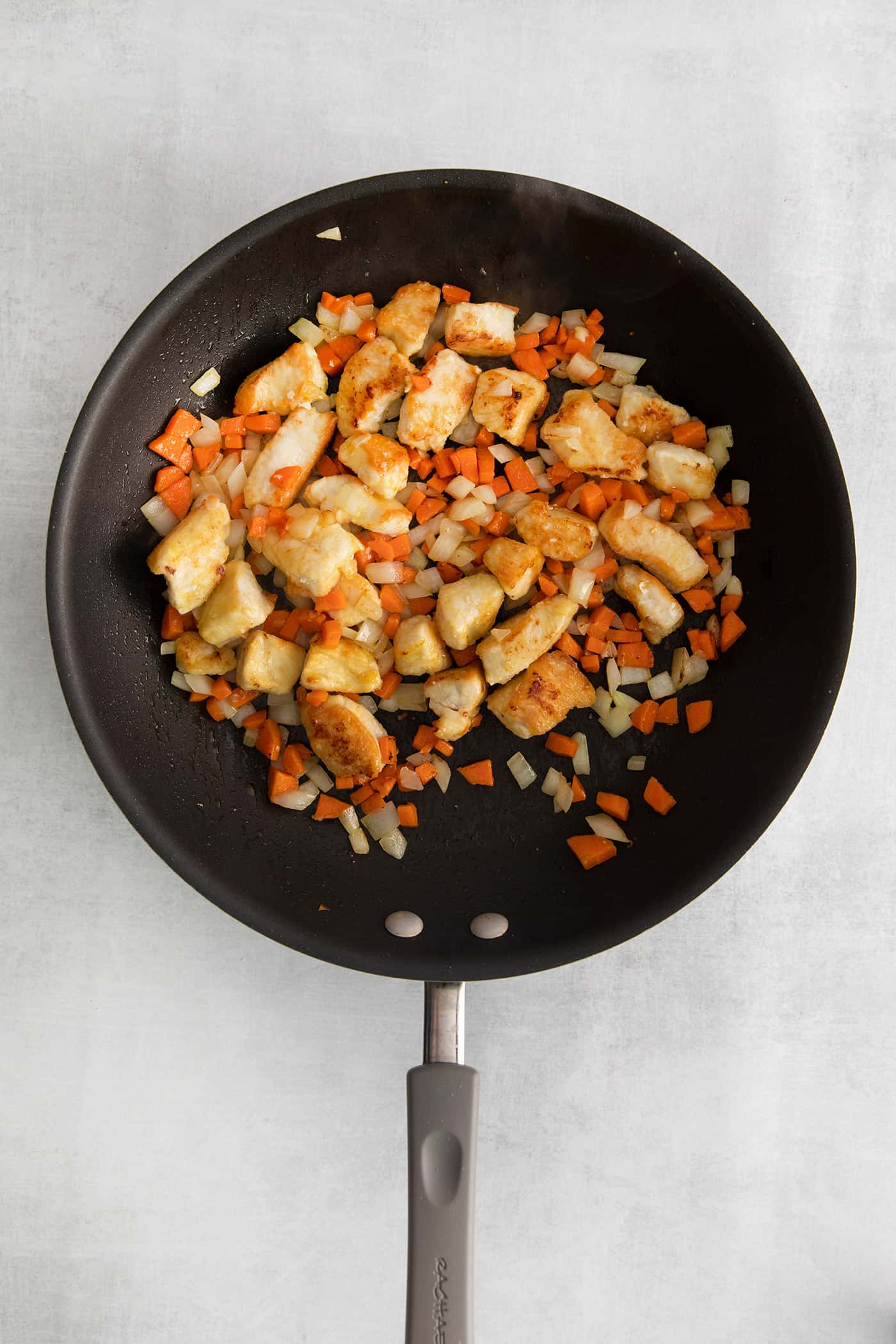 Made with glass noodles, mixed vegetables, and a savory soy glaze, Pad Woon Sen is an easy Thai stir fry that's ready in just 30 minutes! Overhead view of chicken pieces, carrot, and onion in a skillet