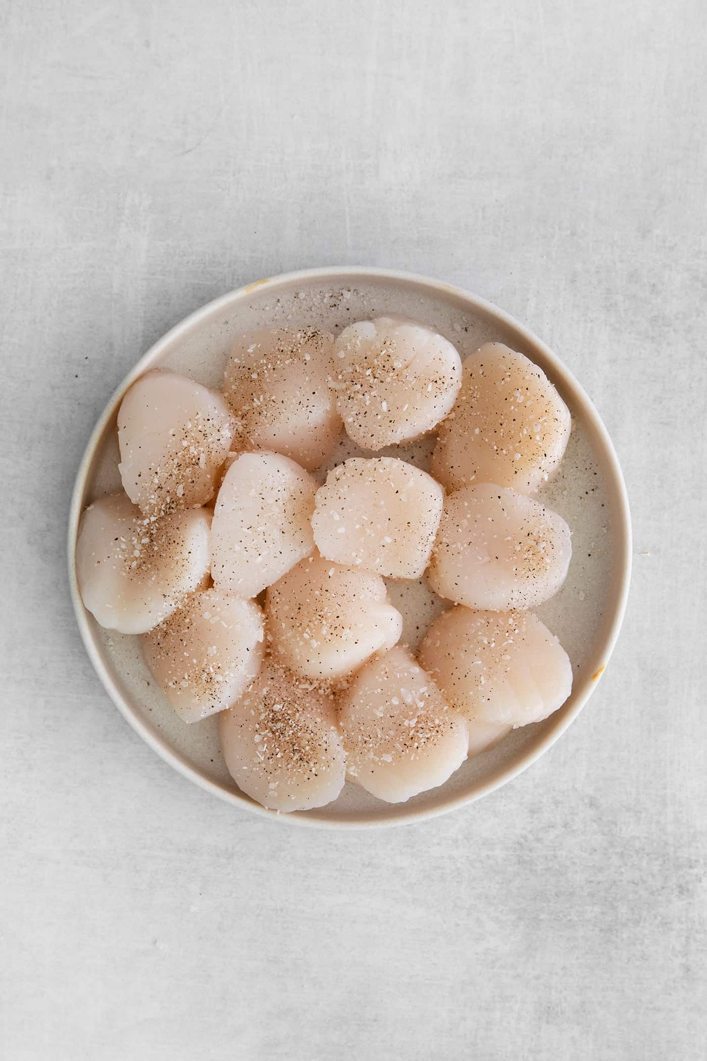 Made with a simple lemon garlic butter sauce, these Pan Seared Scallops are guaranteed to be the highlight of any dinner. Raw sea scallops on a white plate