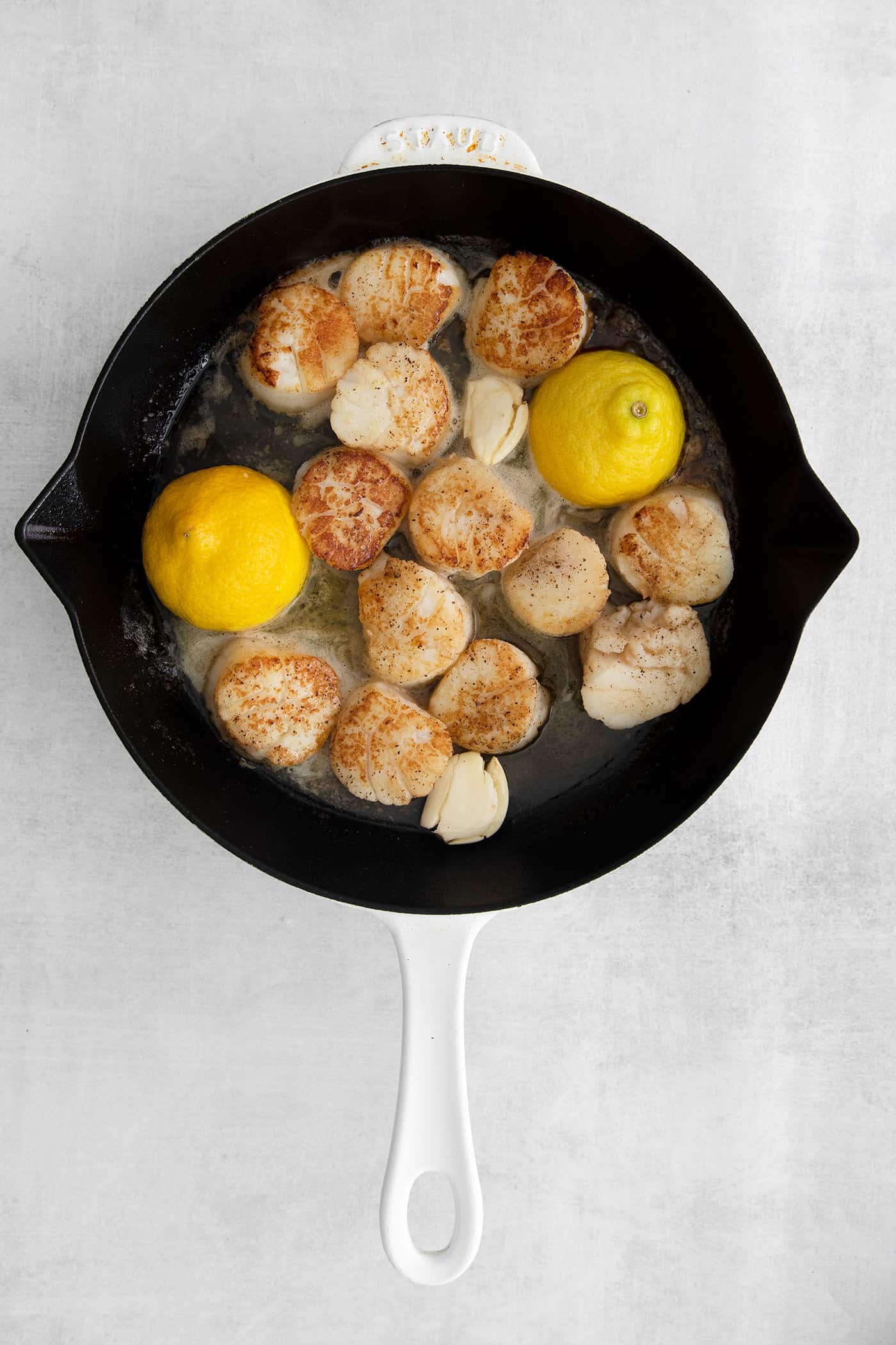 Made with a simple lemon garlic butter sauce, these Pan Seared Scallops are guaranteed to be the highlight of any dinner. Overhead view of seared scallops with lemon in a skillet
